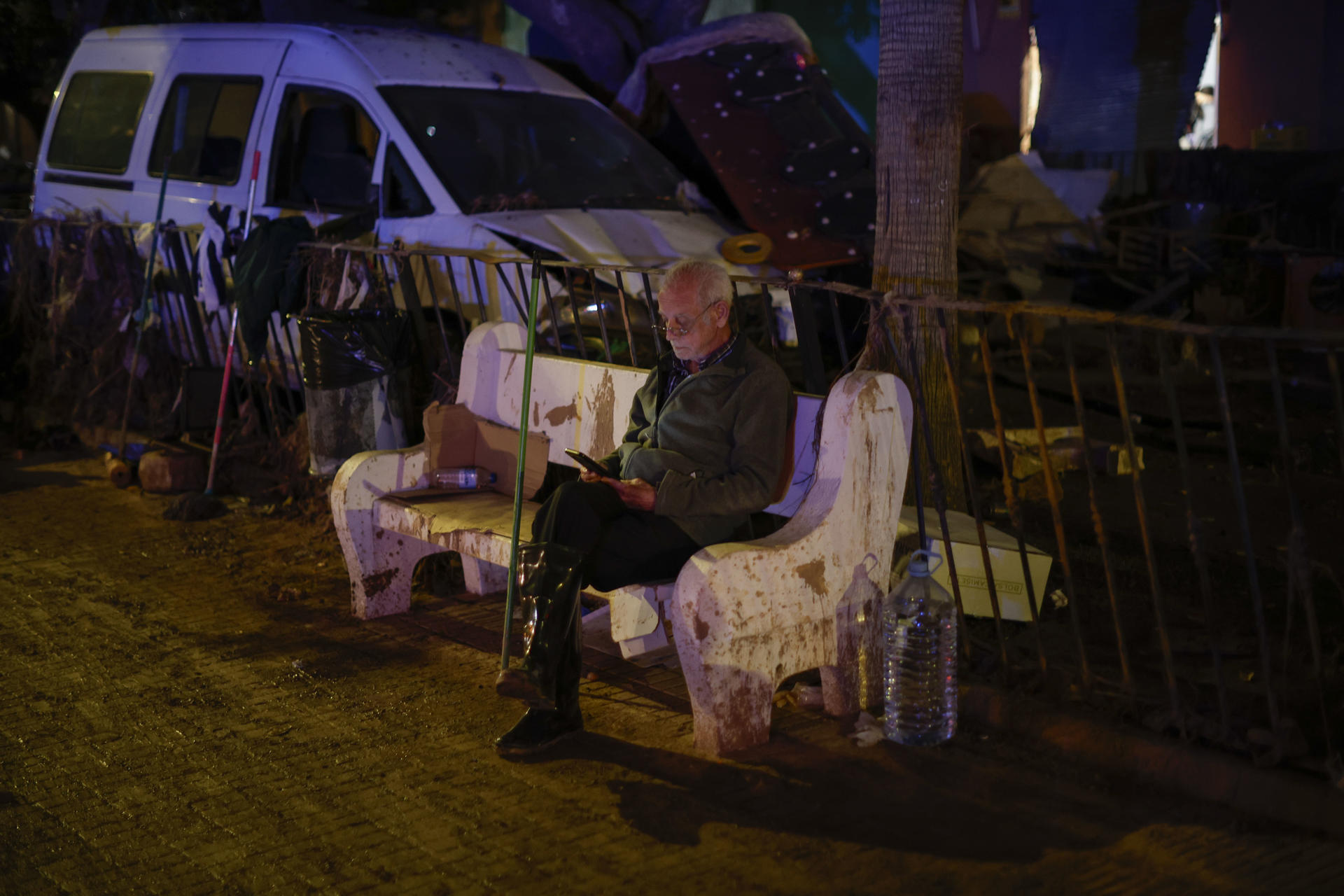 Imagen de un hombre consultando su teléfono en un banco de una calle en Paiporta, días después de la dana en la provincia de Valencia. EFE/ Biel Aliño