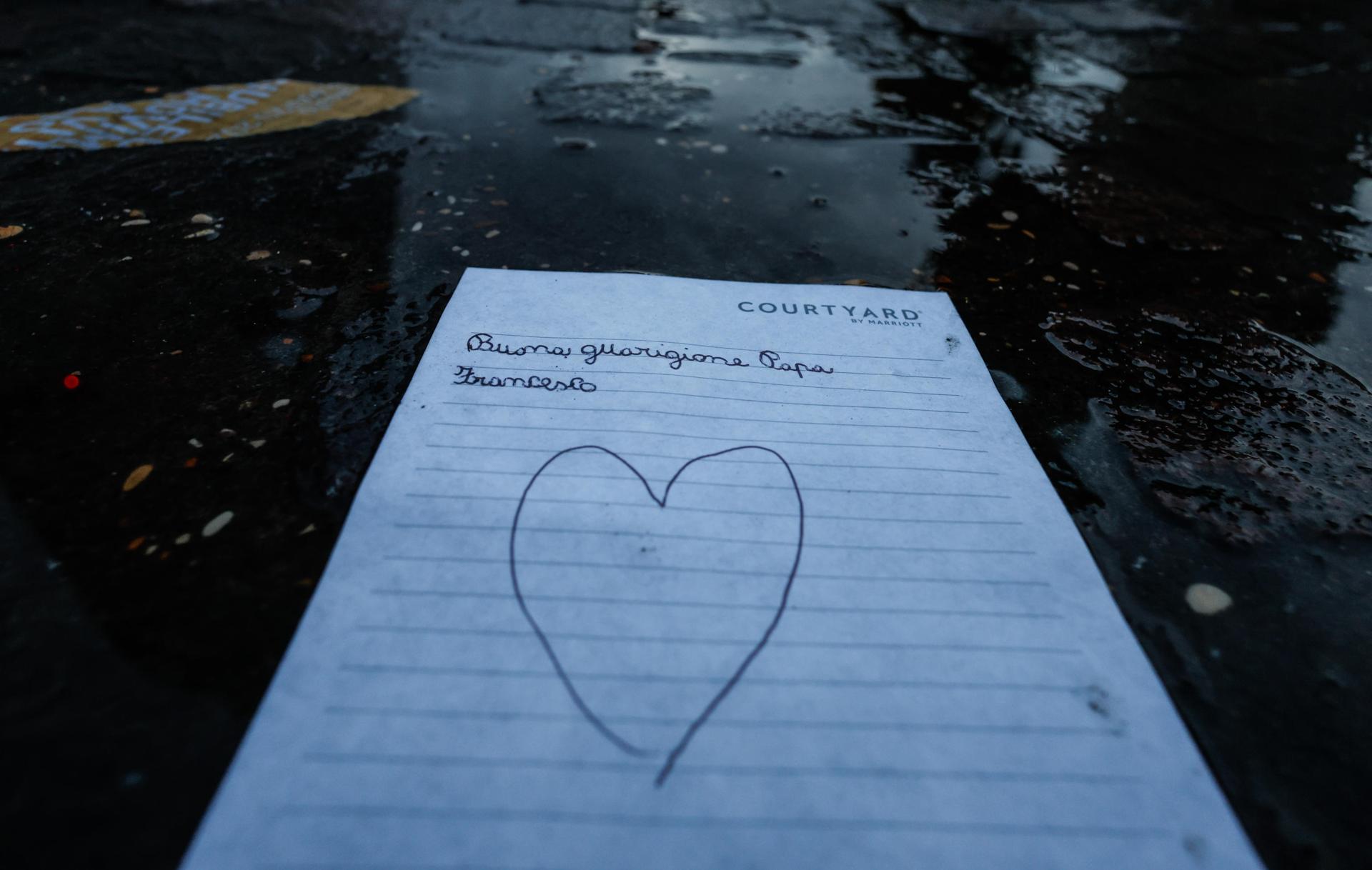 Un dibujo con un corazón colocado en la estatua de Juan Pablo II, a la entrada del Hospital Gemelli, en Roma, donde el papa Francisco está ingresado, le desea una buena recuperación. EFE/EPA/GIUSEPPE LAMI