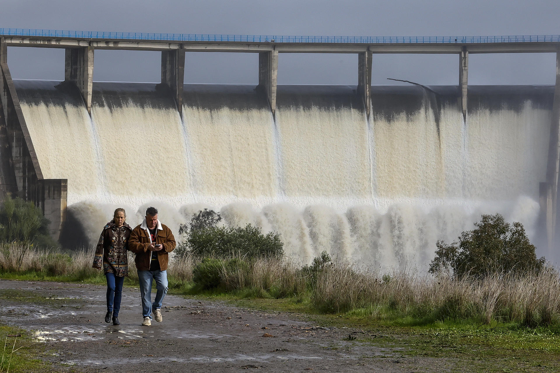 Dos personas pasean junto al embalse de El Gergal en Guillena ( Sevilla) que desembalsa agua tras alcanzar el limite de su capacidad. La última borrasca ha dejado abundante agua en los embalses que abastecen a Andalucía, aunque hay grandes contrastes entre la zona oriental, con el embalse almeriense de Cuevas de Almanzora, al 9,3 % de su capacidad de almacenamiento, y la parte occidental, con el de Melonares (Sevilla), al 104 %.EFE /José Manuel Vidal