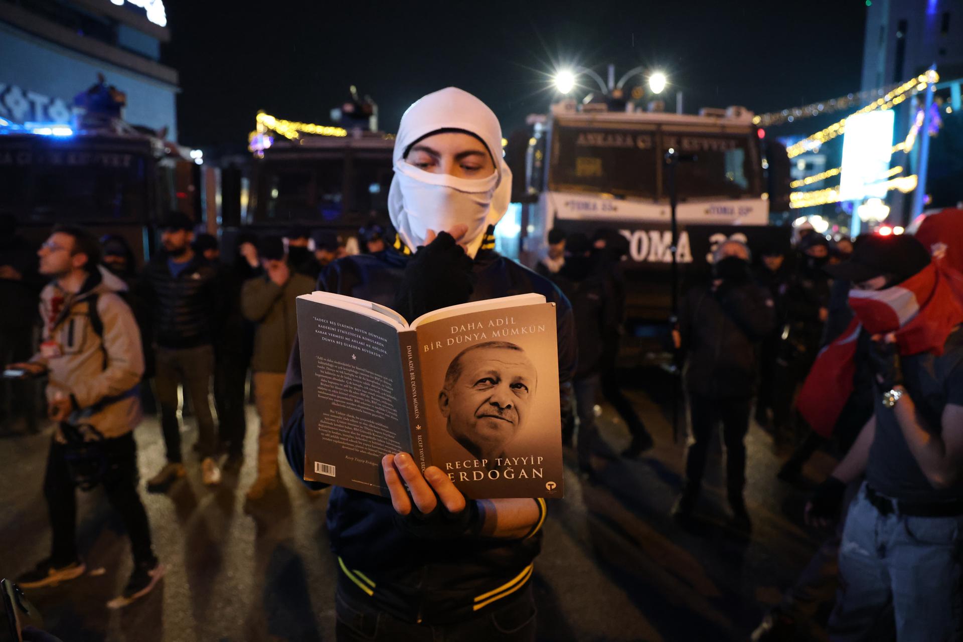 Un manifestante lee el libro de Erdogan frente a las barricadas de la policía antidisturbios turca durante una protesta contra la detención del alcalde de Estambul, Ekrem Imamoglu, en Ankara, Turquía, 24 de marzo de 2025. 
EFE/EPA/NECATI SAVAS