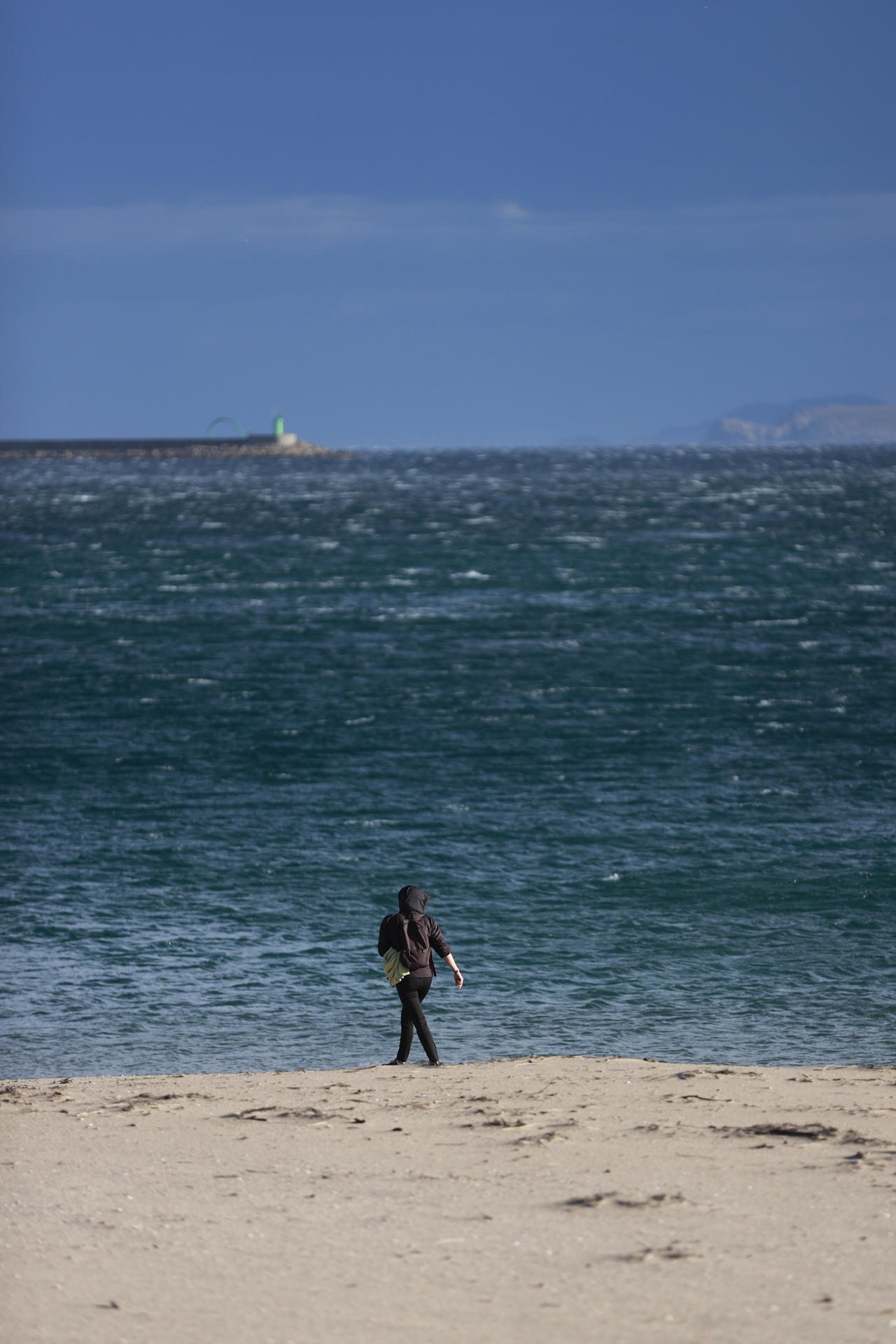 Una mujer camina este jueves por la playa de Santa Cristina, en el concello coruñés de Oleiros, en una jornada marcada por el fuerte viento asociado a la borrasca Martinho, que ha provocado la activación por parte de la Aemet de avisos amarillo o naranja en prácticamente toda Galicia. EFE/Cabalar