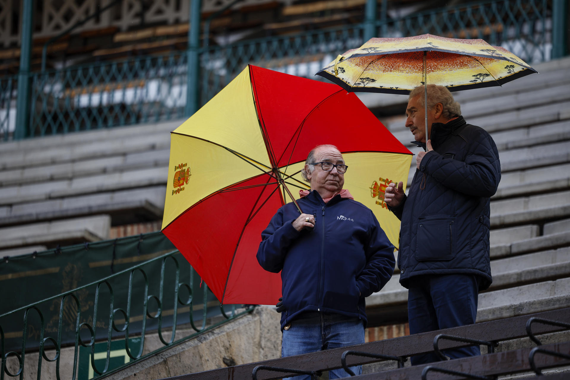 Dos espectadores aguardan protegidos con paraguas en la plaza de toros minutos antes de suspender la primera corrida de toros de la Feria de Fallas a causa de la lluvia. EFE/Biel Aliño