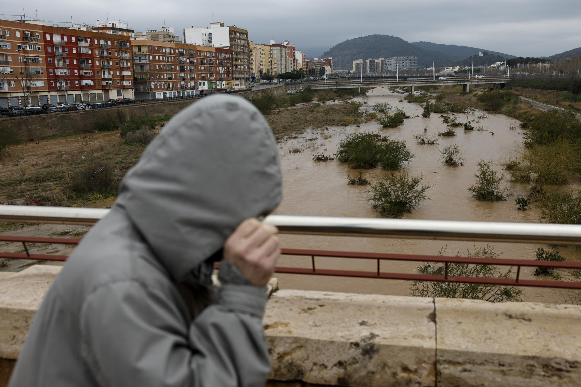 Una persona se protege de la lluvia mientras cruza un puente sobre el río Palancia a su paso por Sagunto cuando varias carreteras de las provincias de Valencia y Castellón permanecen cortadas debido a la lluvia. EFE/Biel Aliño