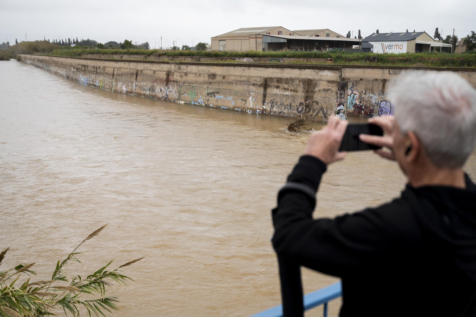 Una persona toma una imágen del río Ana a su paso por Burriana cuando el temporal de lluvias que afecta a la Comunitat Valenciana se mantiene en nivel naranja por lluvias en el interior y litoral norte de la provincia de Castellón y en el interior de Valencia, mientras baja a amarillo en el resto de zonas de ambas provincias. EFE/Andreu Esteban
