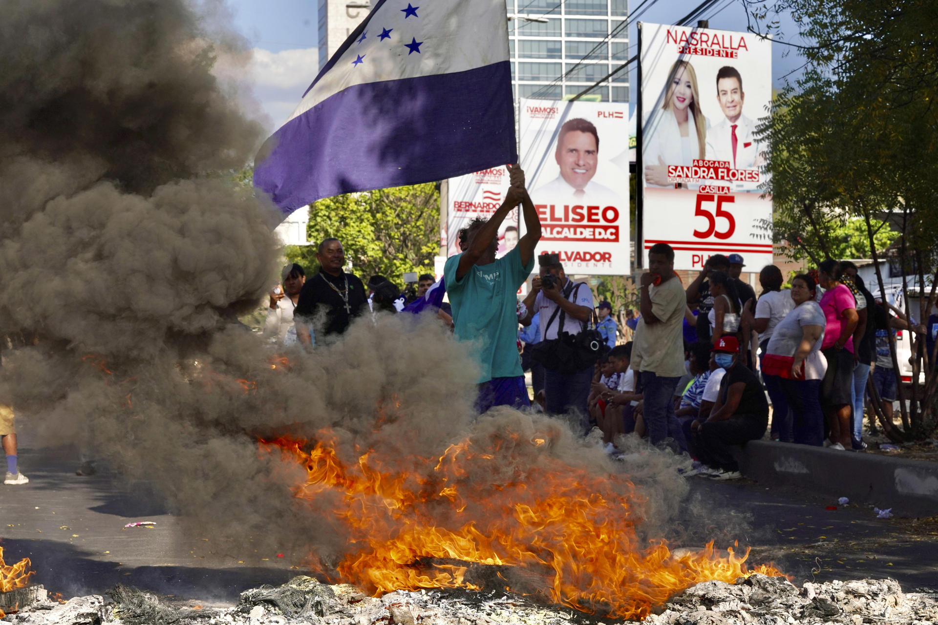 Simpatizantes del Partido Nacional de Honduras ondean banderas y queman llantas en una calle exigiendo que lleguen urnas de votación a su barrio, este domingo en Tegucigalpa (Honduras). EFE/ STR