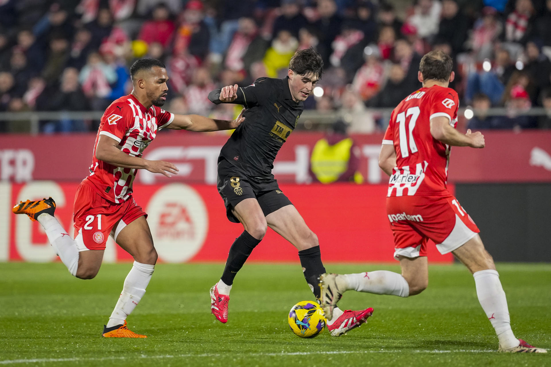 El centrocampista del Valencia Javier Guerra (c) controla e balón ante dos rivales del Girona durante el encuentro correspondiente a la jornada 28 de Laliga EA Sports que disputaron Girona y Valencia en el estadio Montilivi de la capital gerundense. EFE/David Borrat.