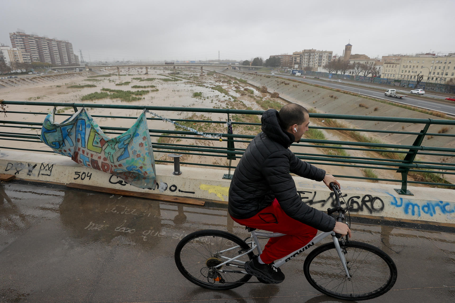 Una persona cruza un puente sobre el nuevo cauce del Turia cuando la lluvia que puede acumular 100 litros por metro cuadrado en doce horas en las provincias de Valencia y Castellón durante este miércoles y mañana jueves, y en todo el episodio de precipitaciones que lleva activo desde el lunes se pueden alcanzar o superar los 400 litros acumulados, especialmente en el interior y prelitoral según la Agencia Estatal de Meteorología (Aemet). EFE/Manuel Bruque