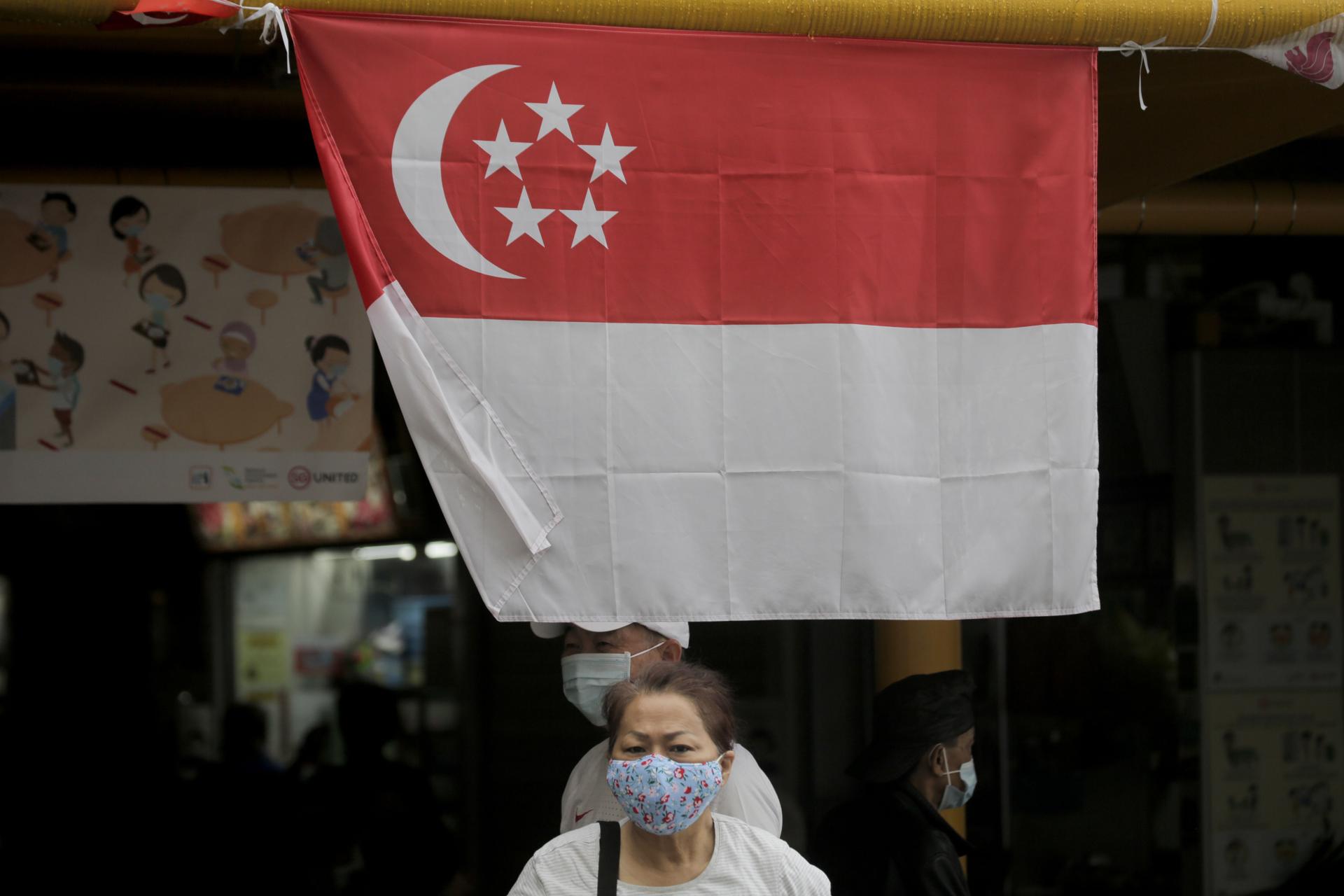 Singapore (Singapore), 08/07/2020.- A woman wearing a mask walks under the Singapore flag ahead of the general elections in Singapore, 08 July 2020. Singaporeans will go to the polls amid the COVID-19 pandemic to vote in the 18th parliamentary general elections where 93 seats will be contested. (Elecciones, Singapur, Singapur) EFE/EPA/WALLACE WOON