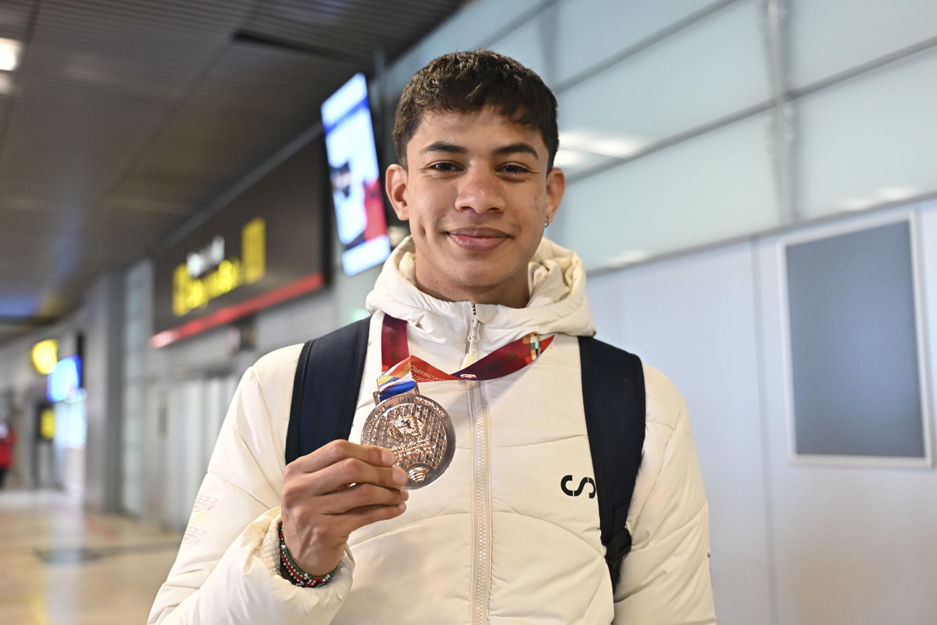 El atleta español Elvin Josué Canales, bronce en 800, muestra su medalla a su llegada a su llegada este martes al aeropuerto de Barajas, Madrid, con el resto del equipo español que ha participado en los Mundiales de Atletismo en pista cubierta de Nankín (China). EFE/ Fernando Villar
