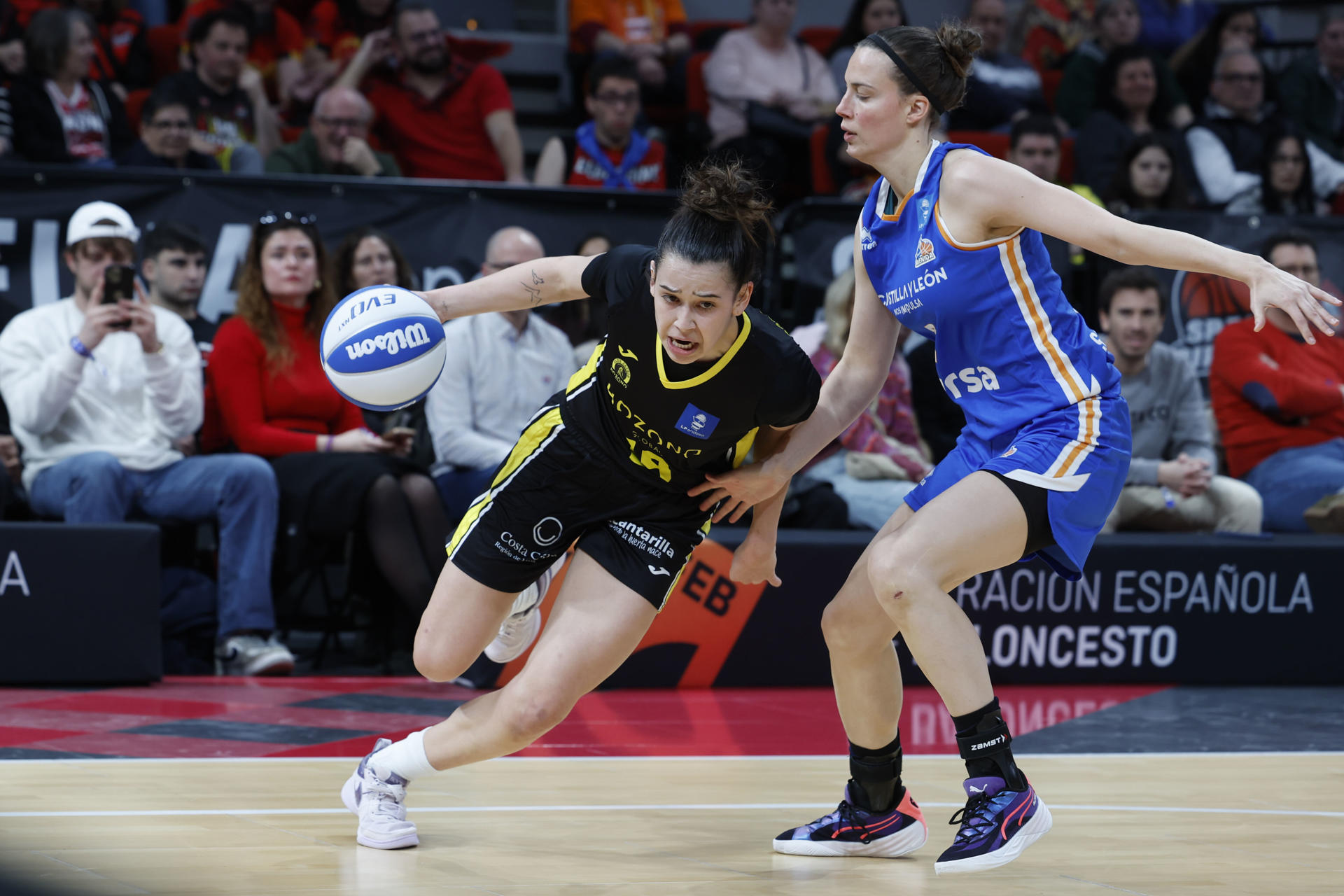 La escolta del Hozono Lou Senechal (i) bota el balón ante la defensa de la alero del Perfumerías Antonia Delaere (d) disputa un balón con la (d) durante la final de la Copa de la Reina de Baloncesto entre el Hozono Jairis y el Perfumerías Avenida, en Zaragoza. EFE/ Javier Cebollada