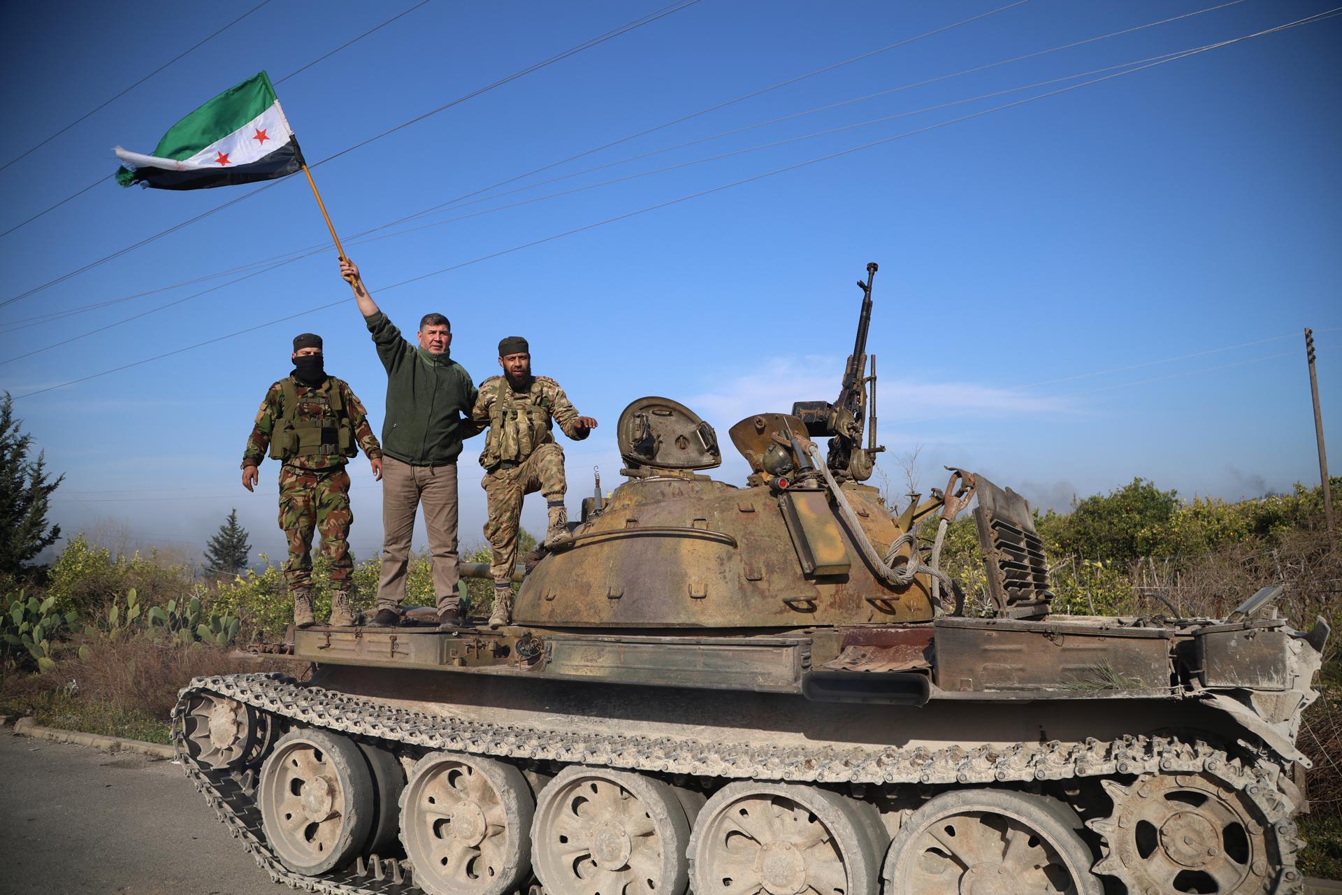 Miembros de las fuerzas de seguridad sirias subidas en un tanque sostienen una bandera siria mientras participan en una operación tras los ataques en Latakia, Siria, el 7 de marzo de 2025. EFE/EPA/BILAL AL HAMMOUD