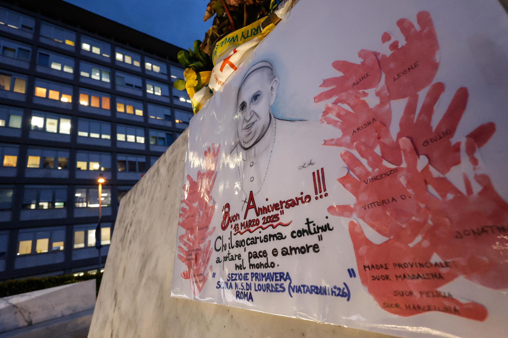 Una pancarta celebra el 12º aniversario del pontificado del papa Francisco colocada junto a la estatua del difunto papa Juan Pablo II, frente al Hospital Agostino Gemelli, en Roma, el 13 de marzo de 2025. EFE/EPA/GIUSEPPE LAMI