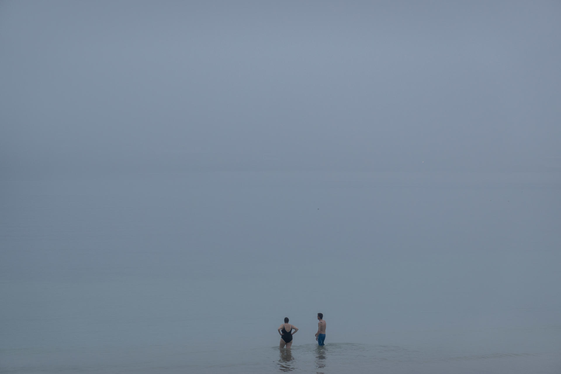 Dos bañistas observan el mar en la playa de Ondarreta de San Sebastián a primera hora de este miércoles, que ha amanecido bajo una densa niebla. EFE/Javier Etxezarreta