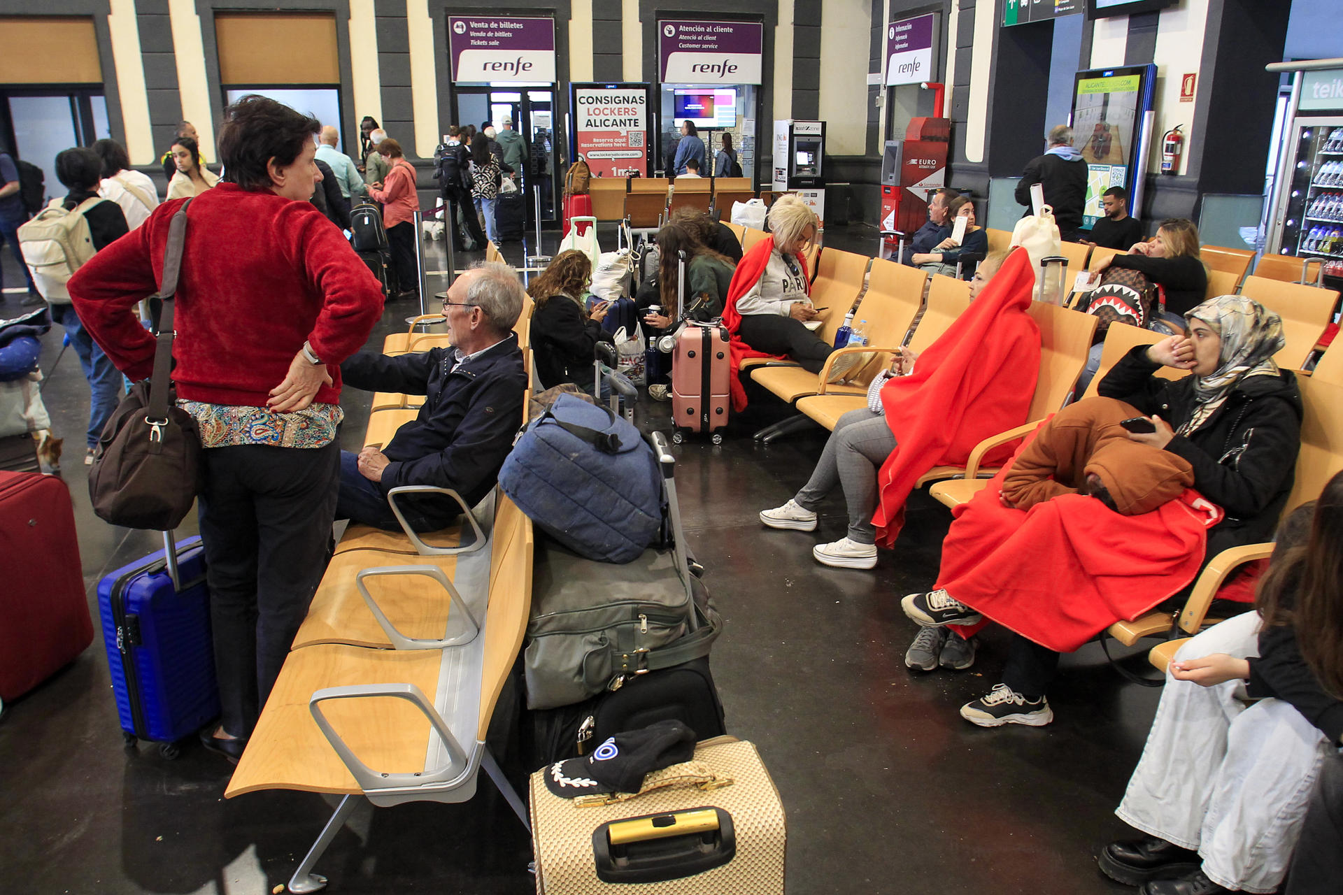 Varios pasajeros aguardan durante la mañana de este martes en la estación de Alicante donde Cruz Roja Comunitat Valenciana ha instalado puntos de atención en para ofrecer respuesta básica a las personas que lo necesiten tras el apagón eléctrico de este lunes. EFE/MORELL