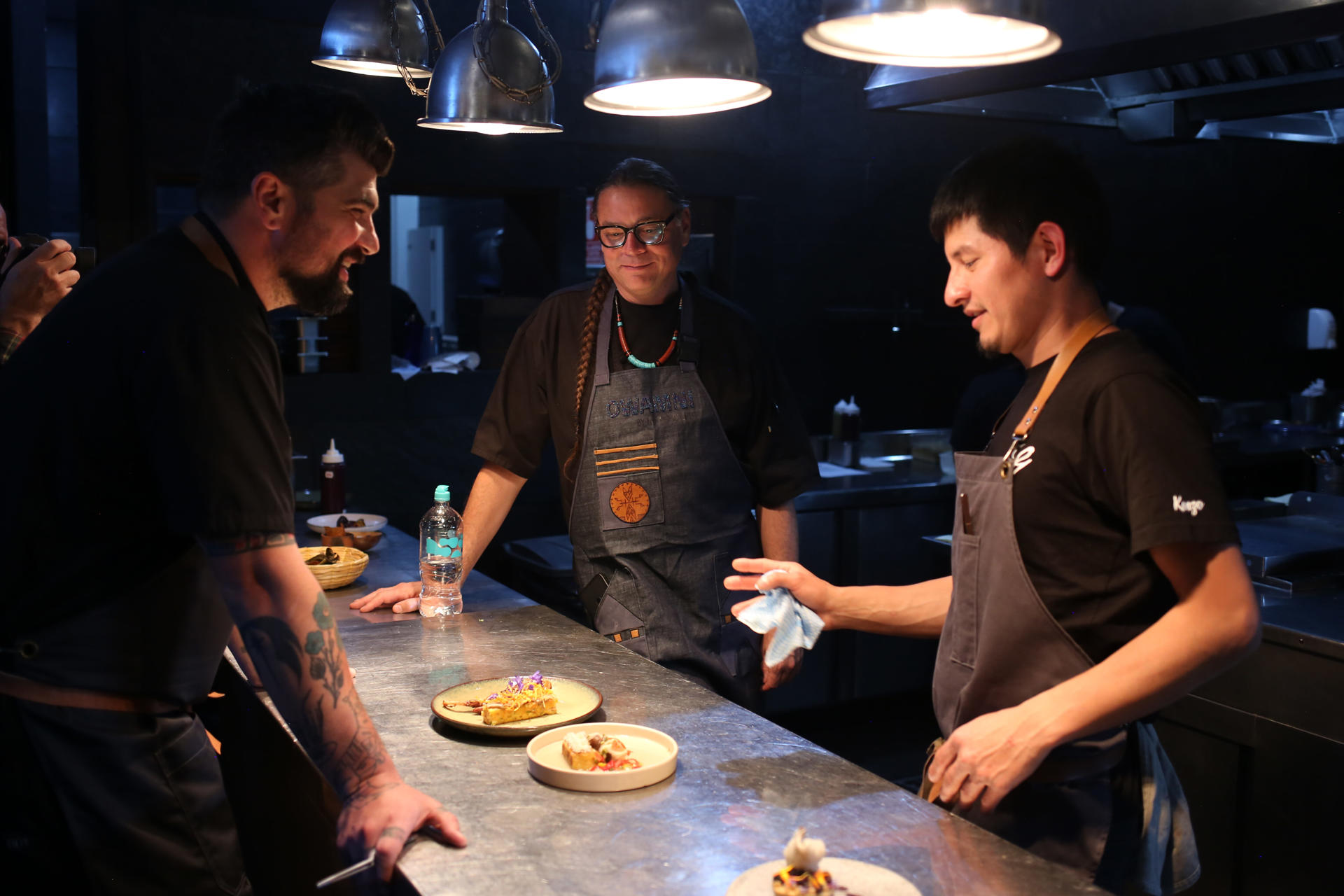 De izquierda a derecha el chef Lee Garman, el chef de la nación Sioux Sean Sherman y el chef boliviano Kenzo Hirose, preparan una plato en la cocina del restaurante Gustu este martes, en La Paz (Bolivia). EFE/Luis Gandarillas