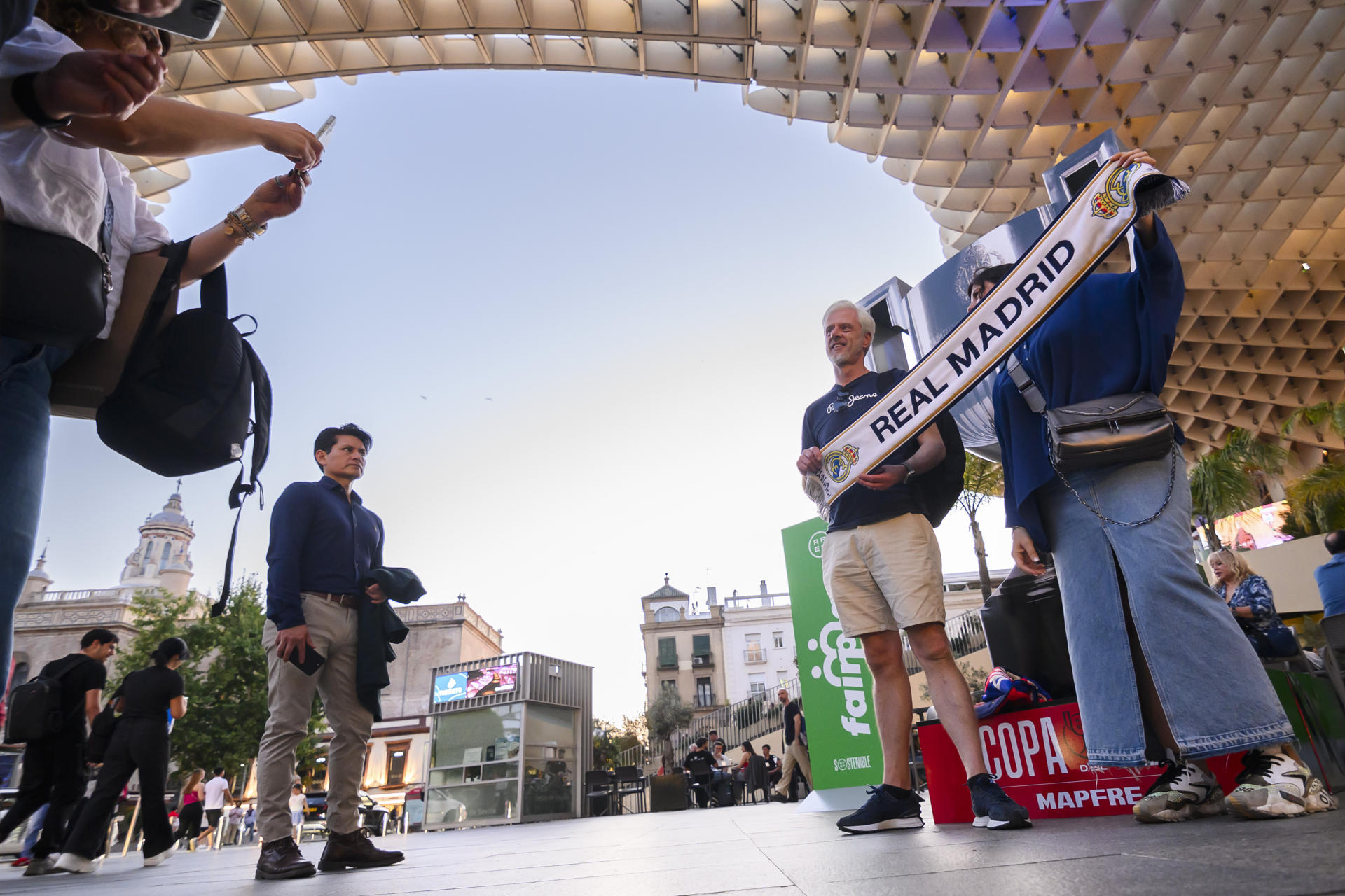 Un grupo de personas con una bufanda del Real Madrid este viernes, en la plaza de La Encarnación de Sevilla la víspera del encuentro de la final de la Copa del Rey que enfrenta al Real Madrid y al FC Barcelona. EFE/ Raúl Caro