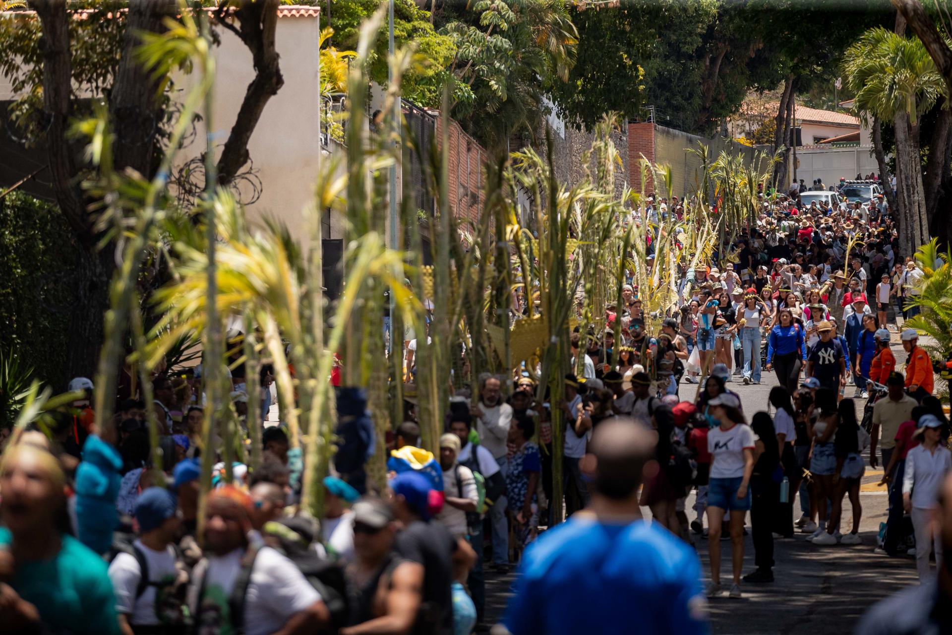 Personas caminan y cargan hojas de palma durante la bajada de los Palmeros de Chacao este sábado, en Caracas (Venezuela). EFE/ Ronald Peña
