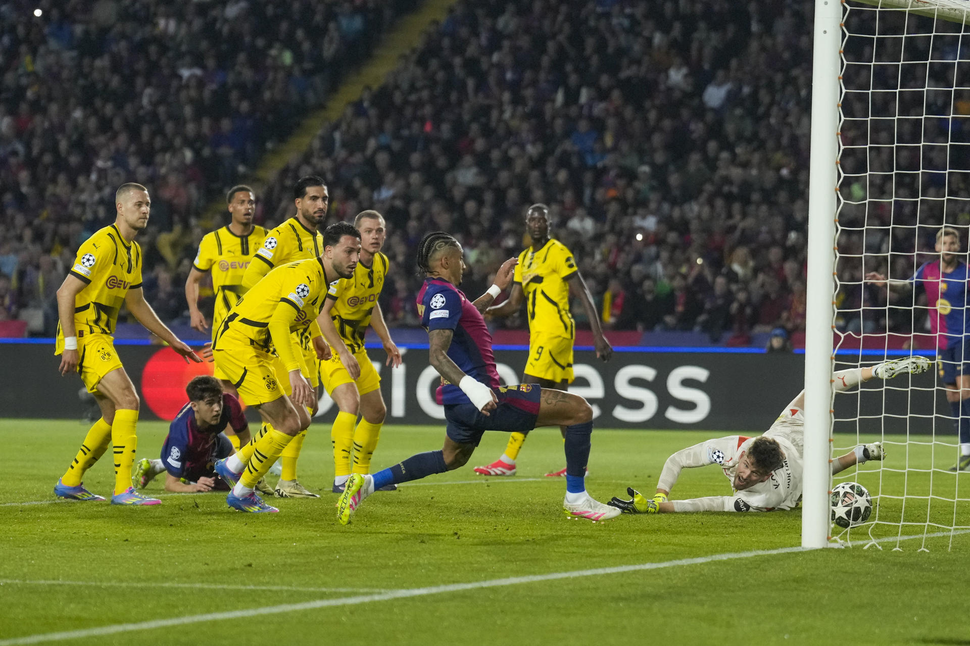 El delantero brasileño del FC Barcelona, Raphinha (2d), intenta rematar el balón ante el guardameta del Borussia, Gregor Kobel, en la jugada que ha significado el primer gol del equipo blaugrana durante el encuentro correspondiente a la ida de los cuartos de final de la Liga de Campeones que disputaron FC Barcelona y Borussia Dortmund en el Estadio Olímpico de Montjuic, en Barcelona. EFE / Enric Fontcuberta