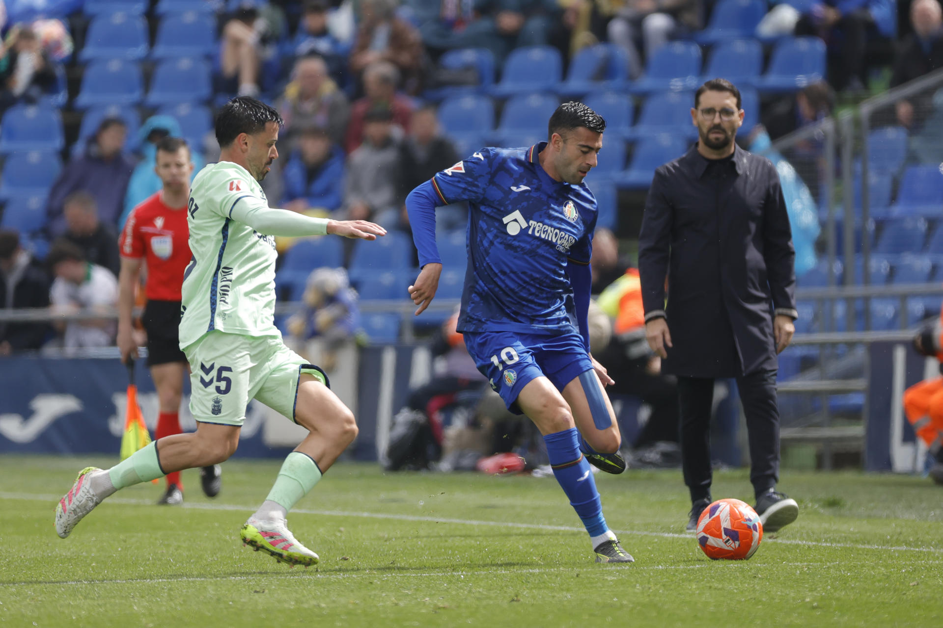 El defensa del Getafe Diego Rico (c) disputa un balón con el centrocampista de Las Palmas Javi Muñoz (i) durante el encuentro de la jornada 31 de LaLiga EA Sports entre Getafe CF y UD Las Palmas, este sábado en el Coliseum de Getafe, en Madrid. EFE/ Zipi