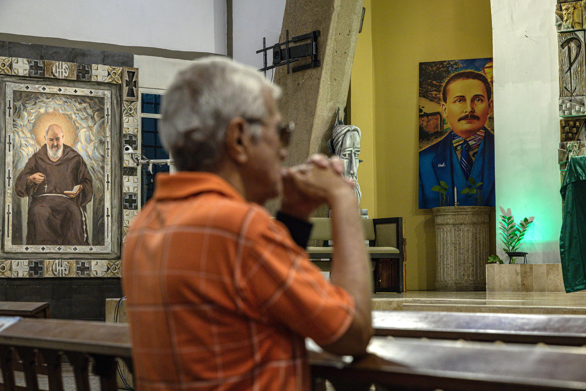 Fotografía de archivo, tomada el pasado 25 de febrero, de un feligrés al orar frente a una imagen del beato católico venezolano José Gregorio Hernández (d), en el interior de la parroquia San Antonio María Claret, en Maracaibo (Venezuela). EFE/Henry Chirinos
