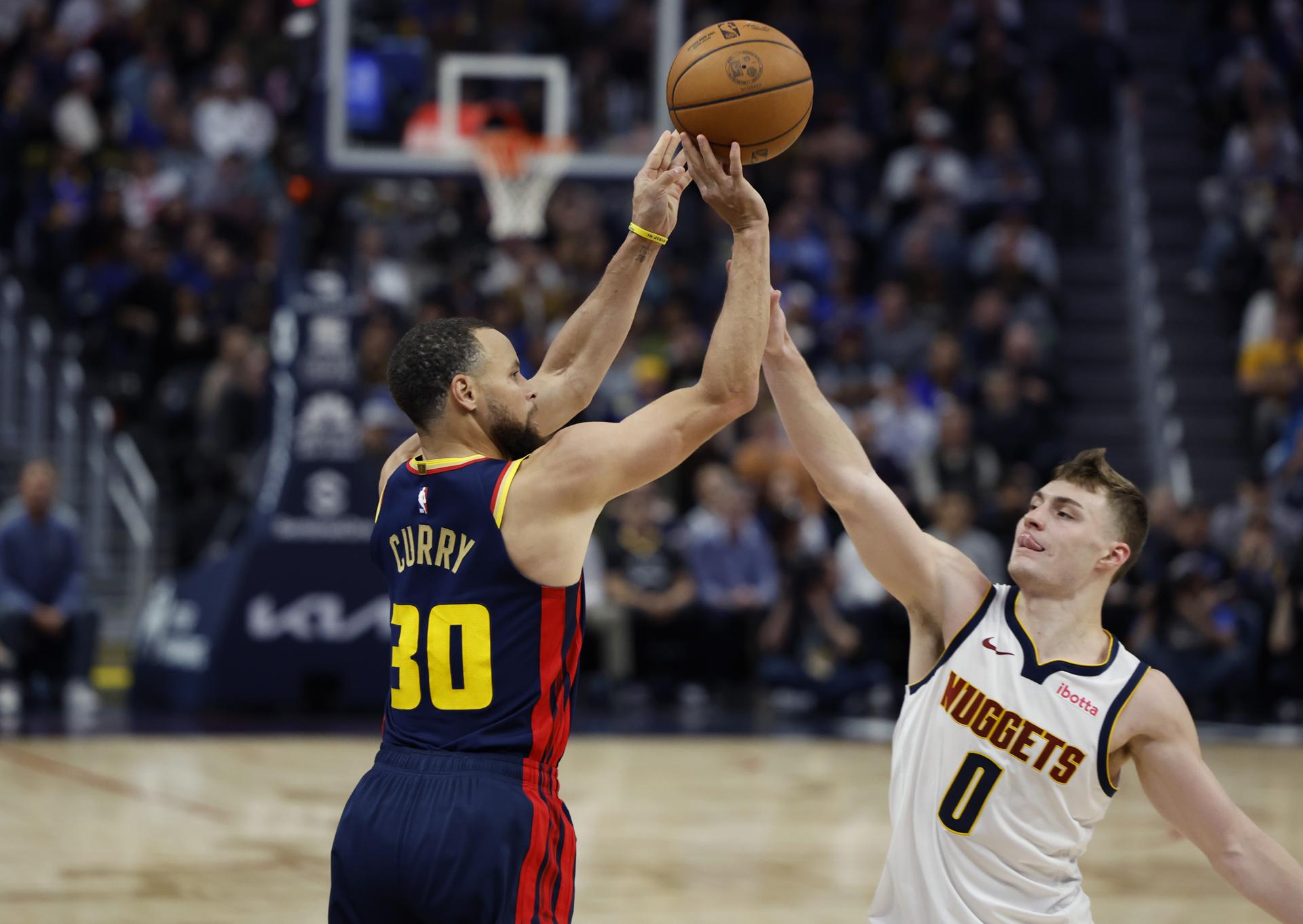 El escolta de los Golden State Warriors, Stephen Curry (izquierda) lanza sobre el escolta de los Denver Nuggets, Christian Braun. EFE/EPA/JOHN G. MABANGLO
