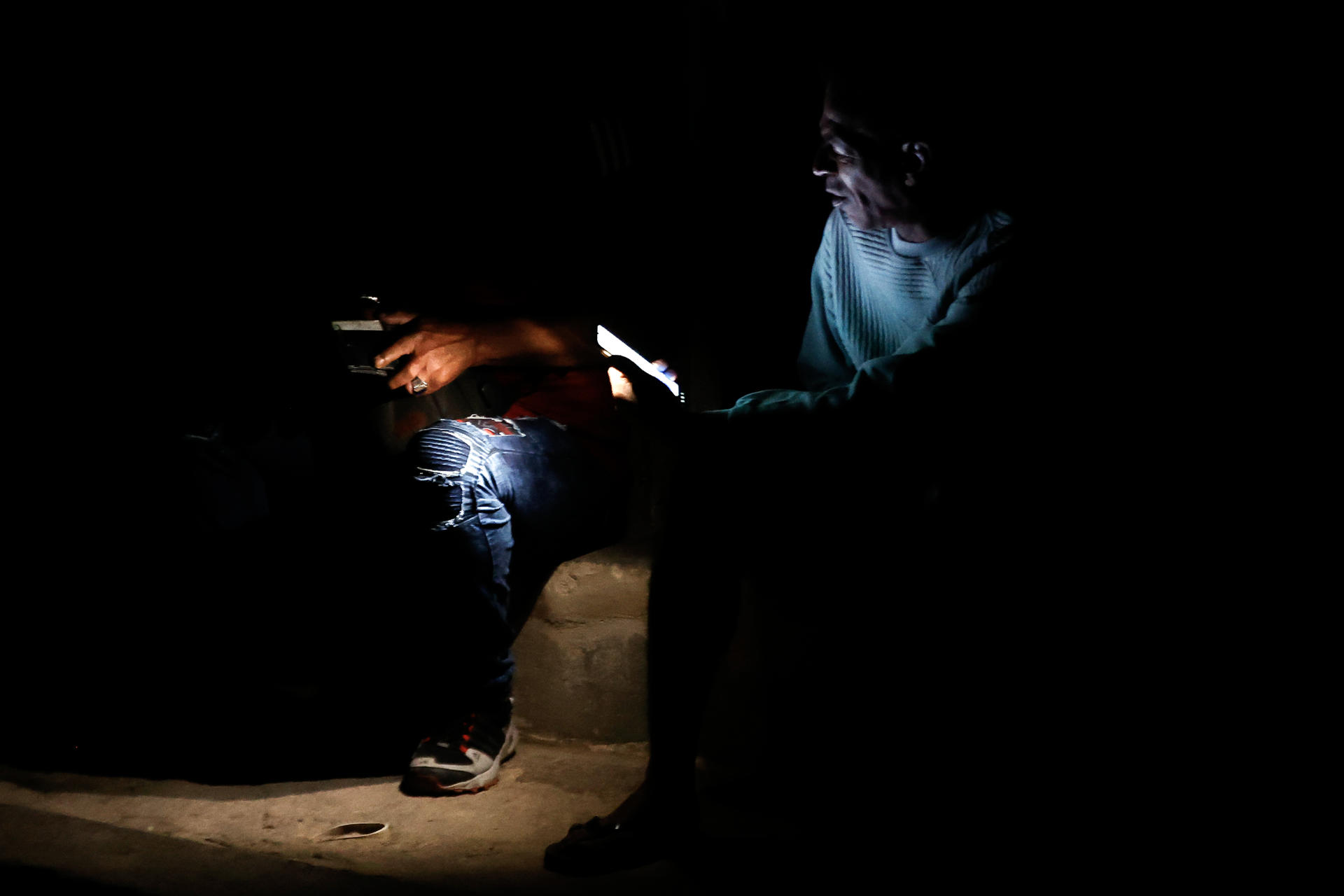 Dos hombres revisan sus teléfonos en un sector sin servicio eléctrico en La Habana (Cuba), en una fotografía de archivo. EFE/ Ernesto Mastrascusa