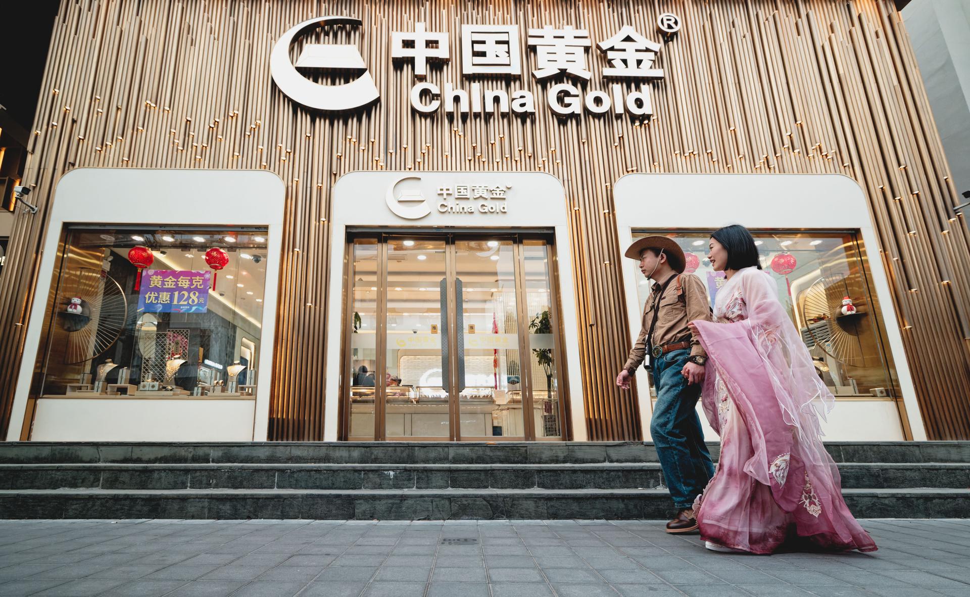 Una pareja pasa por delante de un punto de venta de oro, en Shanghái (China), este miércoles. EFE/ Alex Plavevski