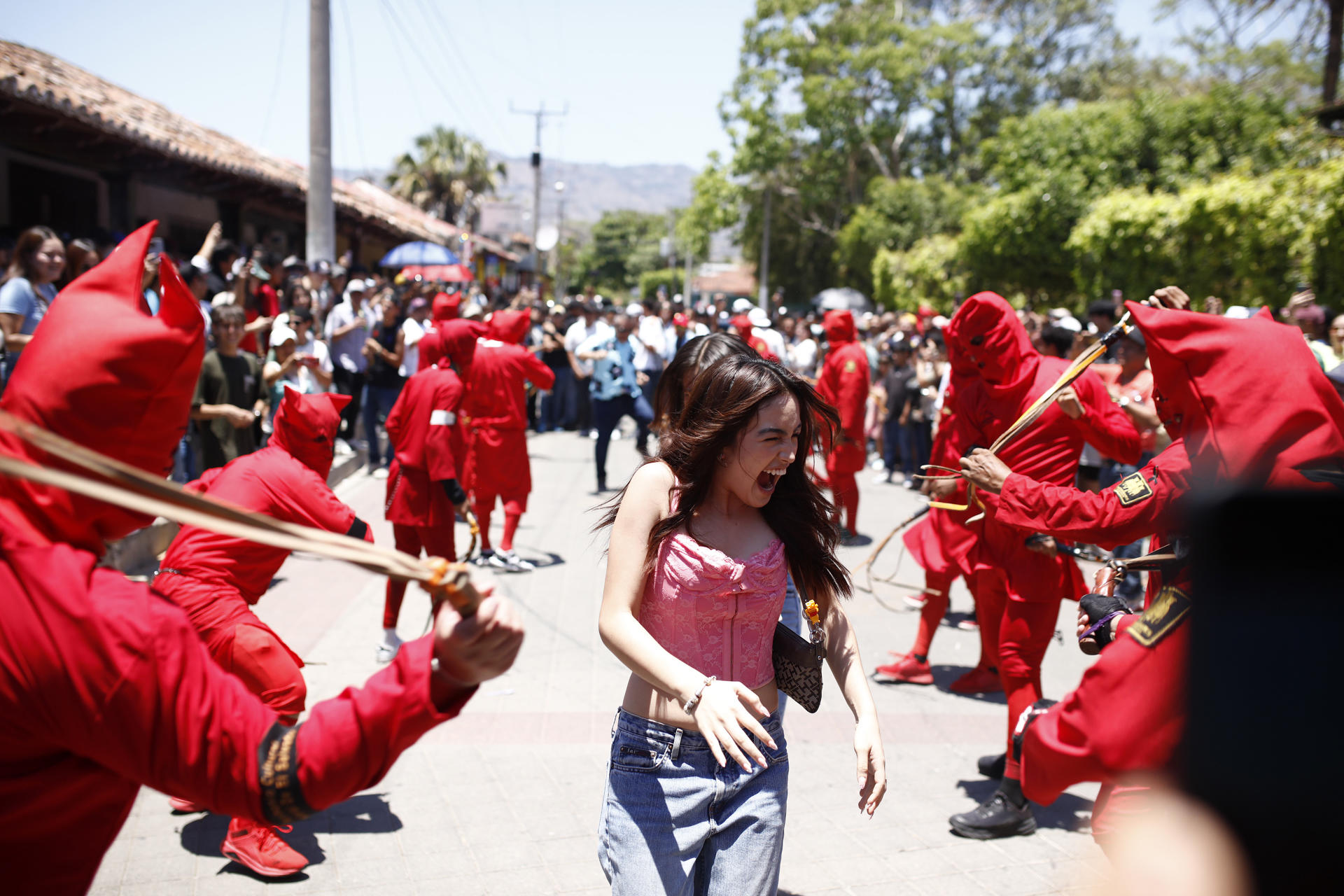 Una joven al pasar en medio de un grupo de talcigüines, que en náhuatl significa hombres endiablados, al participar este lunes, 14 de abril, durante una celebración tradicional de la Semana Santa, en Texistepeque (El Salvador). EFE/Rodrigo Sura