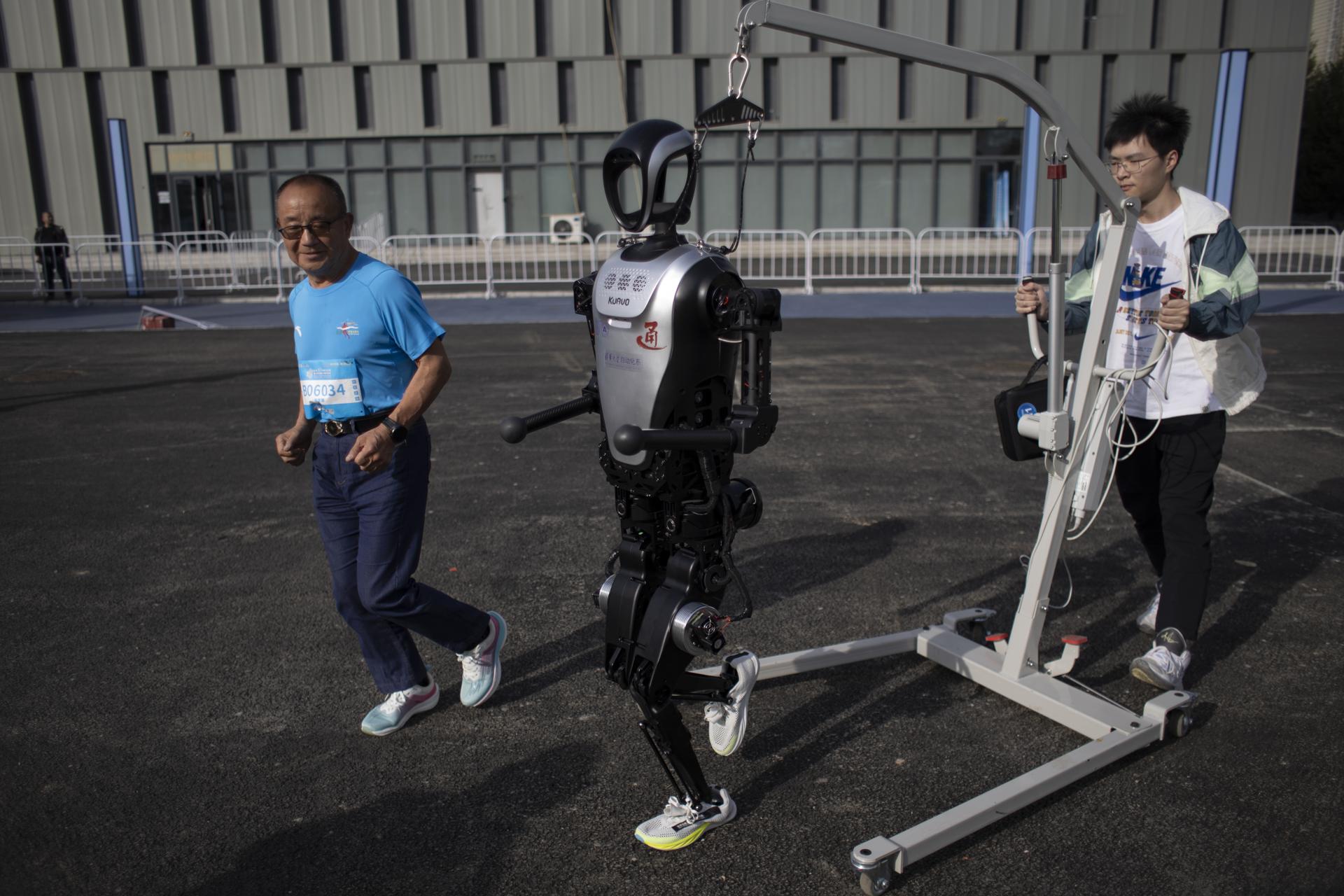 Zhang Xianhua (71 años), un corredor que participará en la carrera, trota junto a un robot humanoide antes de una carrera entre humanos y robots en Pekín. EFE/EPA/ANDRÉS MARTÍNEZ CASARES