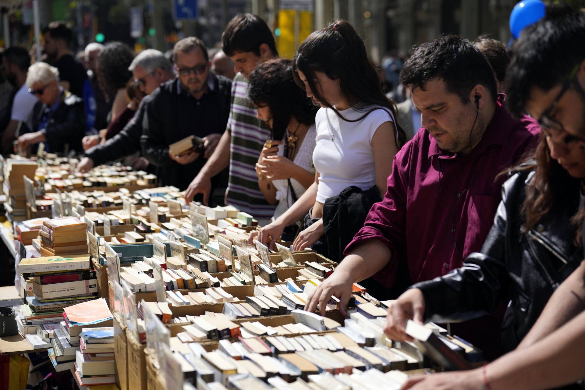 Varias personas buscan libros en una parada en el Paseo de Gracia de Barcelona durante la Diada de Sant Jordi, en la que los catalanes toman las calles a la búsqueda de libros y rosas para regalar a sus seres queridos y allegados. EFE/Alejandro García