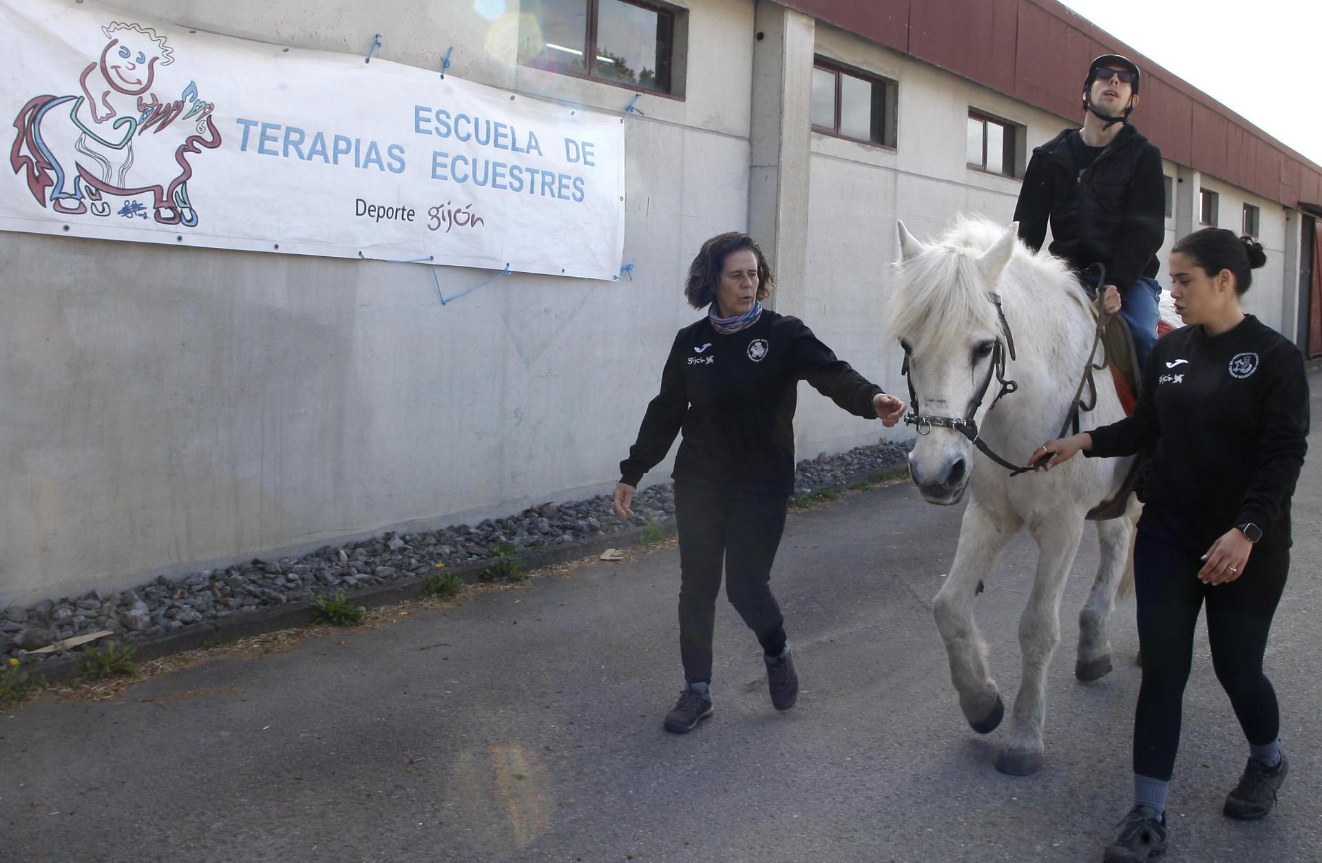 Interactuar con caballos, una actividad que desde el siglo pasado se conoce como equinoterapia que ha demostrado efectos beneficiosos en la rehabilitación neuromuscular y el desarrollo emocional en casos de daño cerebral, se utiliza cada vez más y amplía su campo de acción en personas con depresión y en víctimas de violencia machista. Un joven de 30 años con parálisis cerebral monta un caballo asistido por dos monitoras durante una sesión de equinoterapia en el centro ecuestre de Gijón. EFE/Juan González