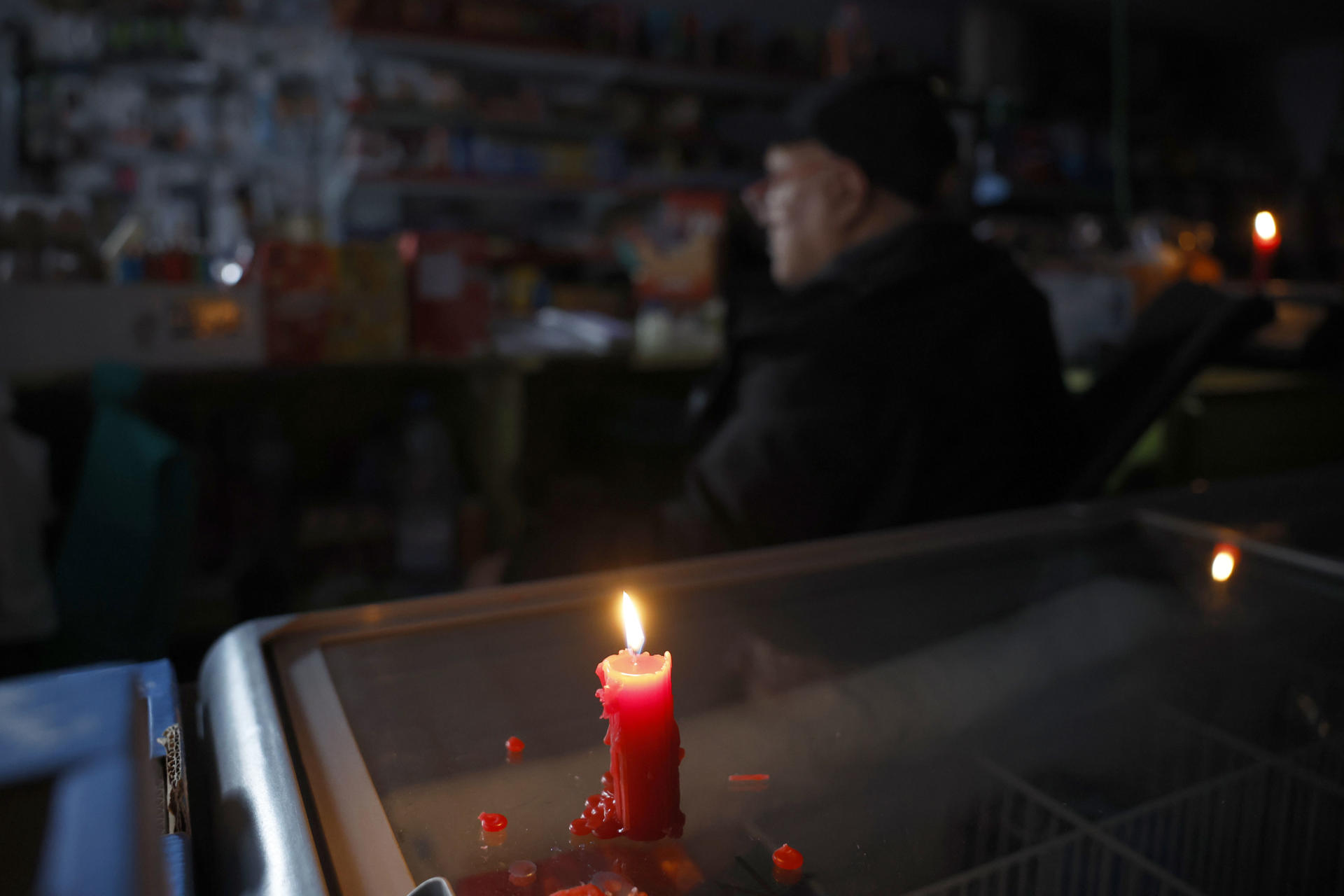 El dependiente de un supermercado se ilumina con una vela durante el corte de suministro eléctrico que afecta este lunes a España y que ha dejado sin servicio el metro y el tranvia de Barcelona y todas las líneas de ferrocarril en Barcelona, y sin red de teléfonos móviles ni internet. EFE/Alberto Estévez