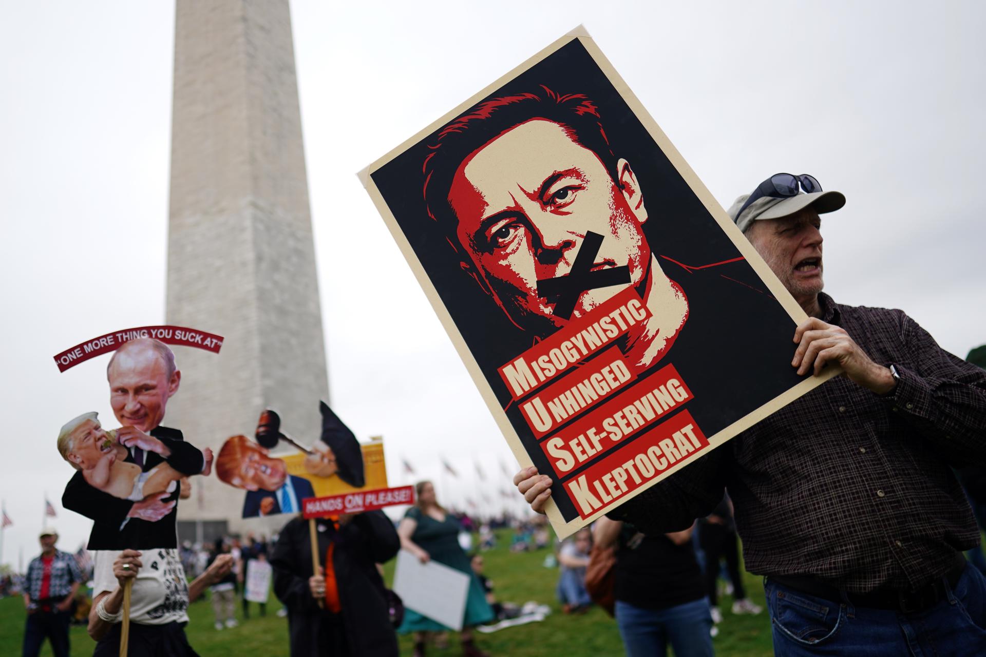Un manifestante sostiene un cartel que representa a Elon Musk con el texto '¡Manos afuera!' en el National Mall en Washington, DC, EE. UU. EFE/WILL OLIVER