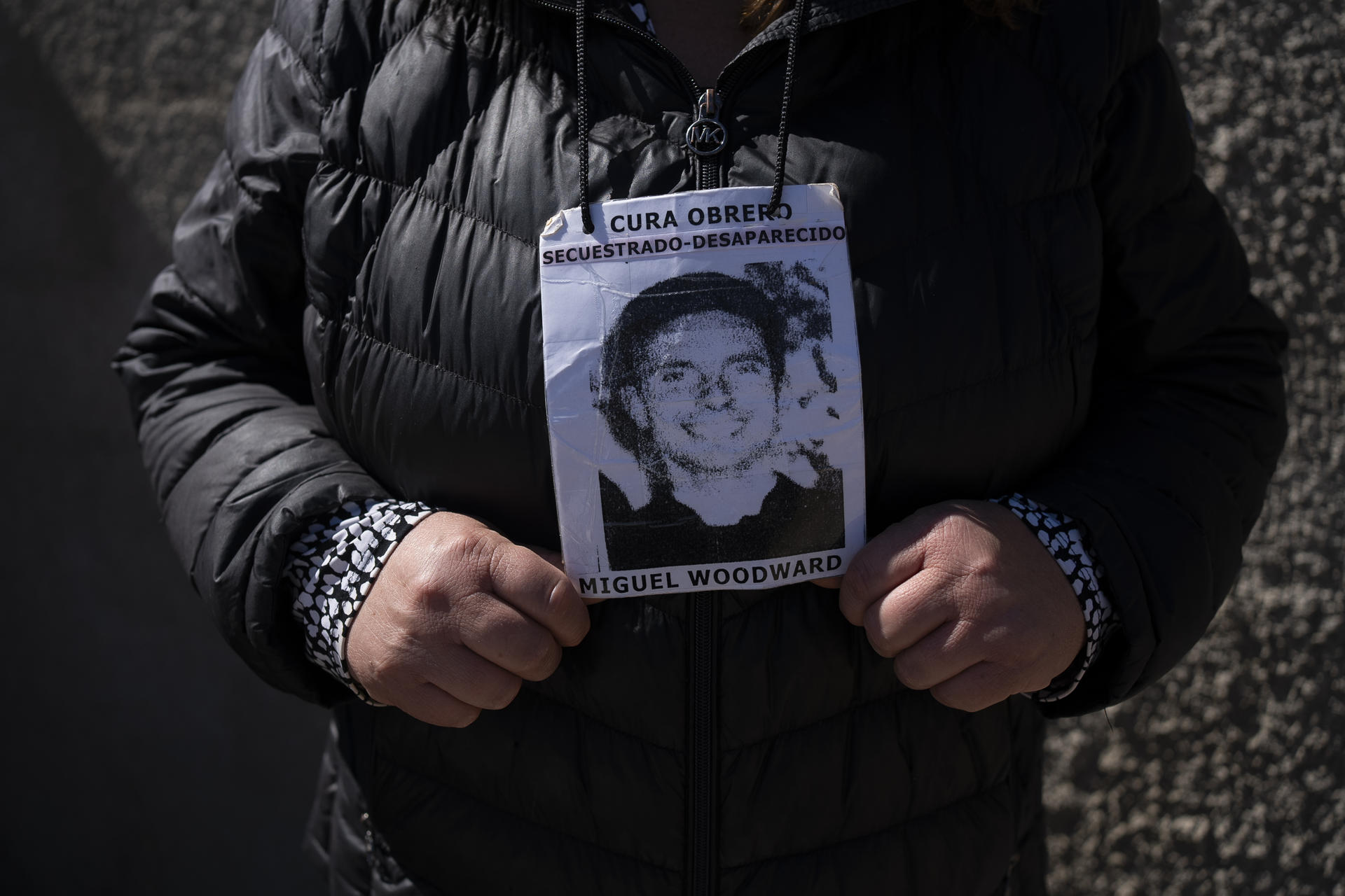 Detalle del tronco de una mujer que porta una fotografía del sacerdote católico chileno británico Miguel Woodward, quien fue asesinado y desaparecido por agentes de la dictadura pocos días después del golpe de Estado de Augusto Pinochet en 1973 y de quien buscan sus restos en el Cementerio N°3 de Playa Ancha, en Valparaiso (Chile). EFE/Adriana Thomasa