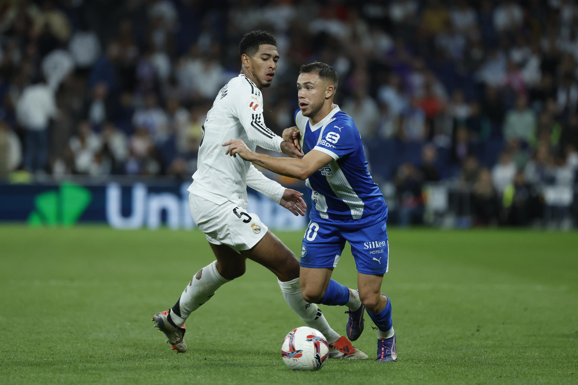El delantero argentino del Alavés, Tomás Conechny (d), se lleva el balón ante el centrocampista inglés del Real Madrid, Jude Bellingham, durante el encuentro correspondiente a la séptima jornada de Laliga EA Sports que Real Madrid y Alavés disputaron en el estadio Santiago Bernabéu, en Madrid. EFE / Juanjo Martín.