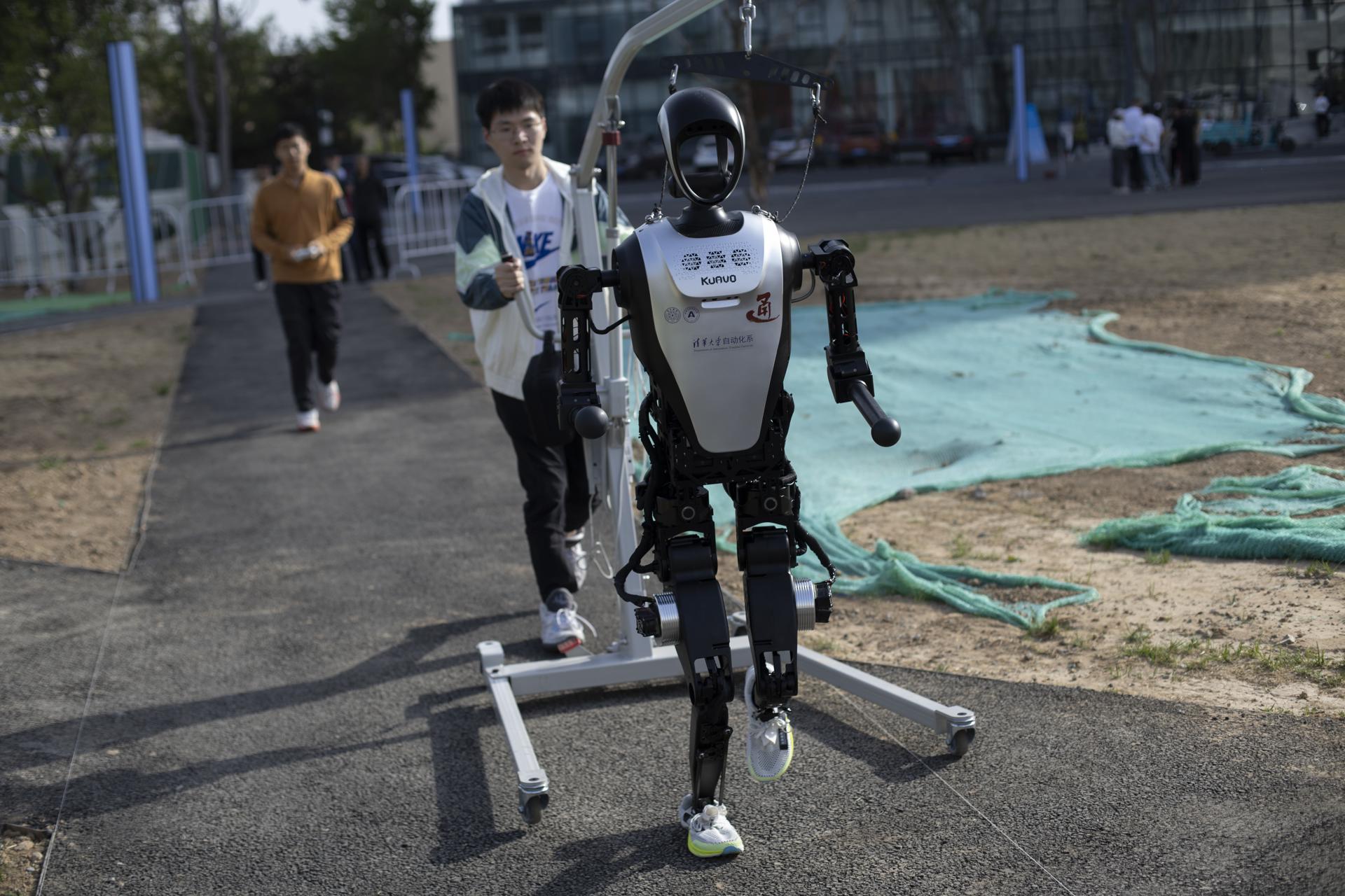 Un técnico camina detrás de un robot humanoide antes de la carrera de humanos y robots en Pekín. EFE/EPA/ANDRÉS MARTÍNEZ CASARES