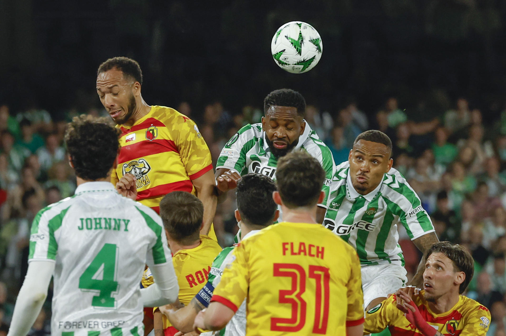 El delantero del Betis Cédic Bakambu (c) cabecea un balón ante su compañero Natan Bernardo de Souza (d) y Enzo Ebosse (i), del Jagiellonia Bialystok, durante el partido de ida de los cuartos de final de la Liga Conferencia que Real Betis y Jagiellonia Bialystok disputan este jueves en el estadio Benito Villamarín, en Sevilla. EFE/Julio Muñoz
