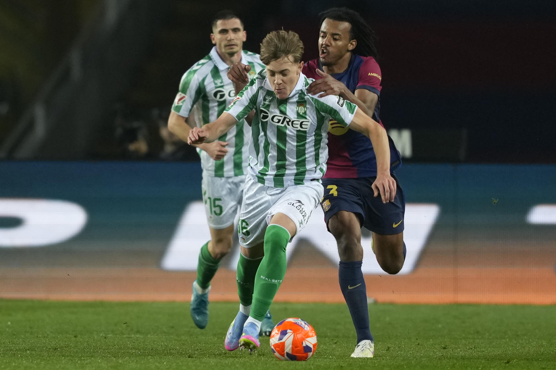 El centrocampista del Betis, Jesús Rodriguez (i), se lleva el balón ante el defensa francés del FC Barcelona, Jules Koundé, durante el encuentro correspondiente a la jornada 30 de Laliga EA Sports que disputan hoy sábado FC Barcelona y Betis en el Estadio Olímpico Lluis Companys de Barcelona. EFE / Alejandro Garcia