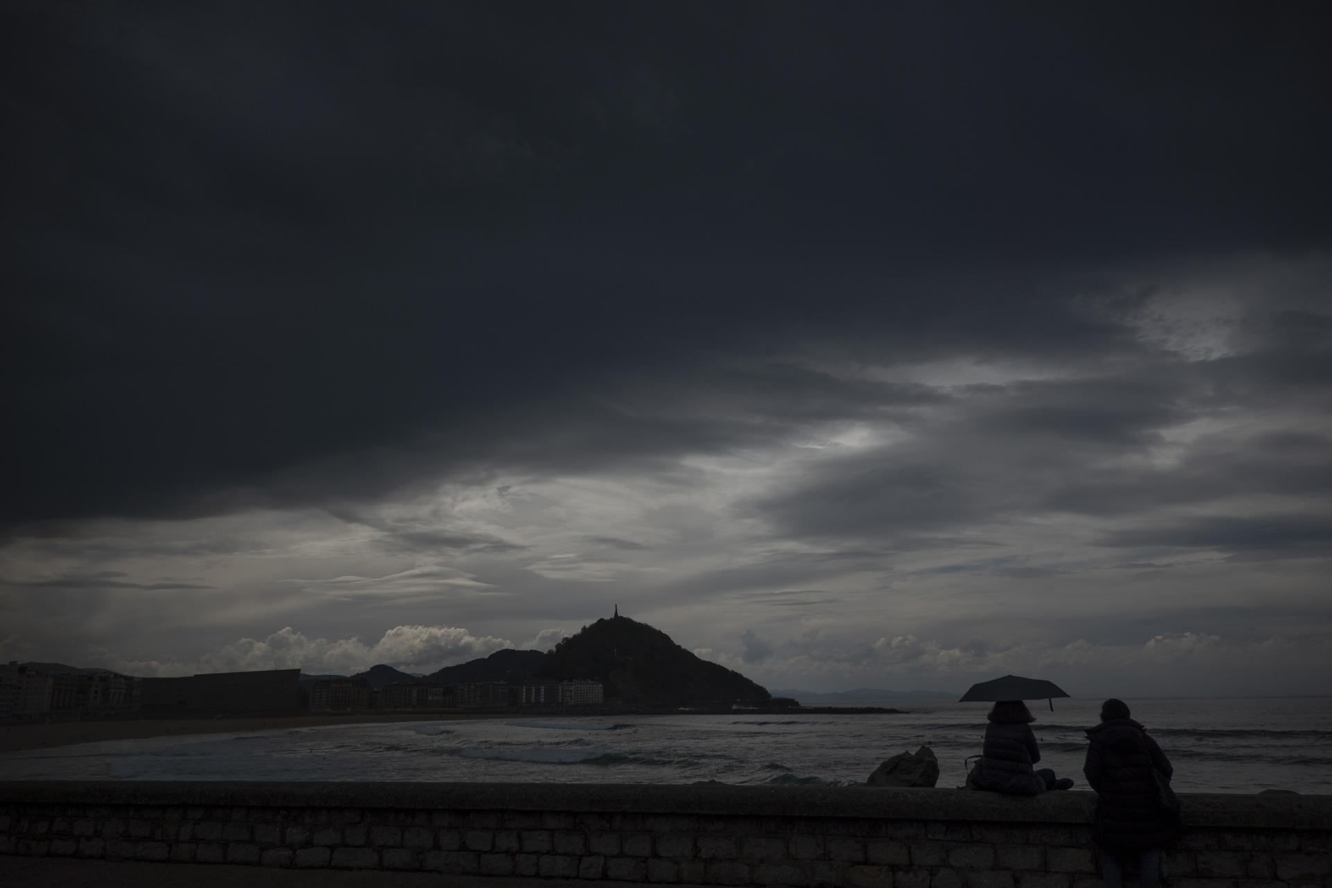 Unas mujeres observan la playa de la Zurriola de San Sebastián bajo un cielo lleno de nubes de tormenta. EFE/Juan Herrero