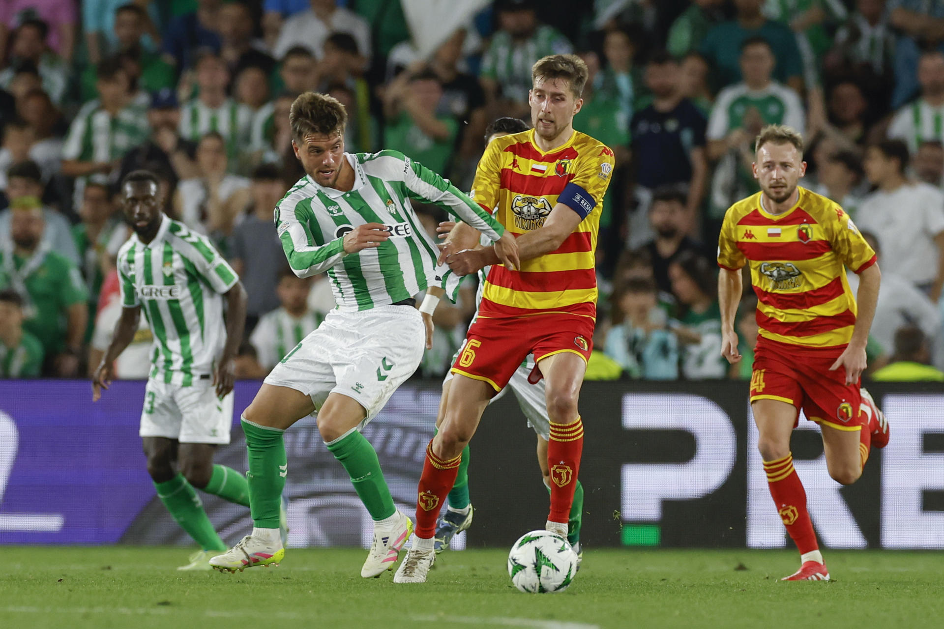 El centrocampista del Betis Giovani Lo Celso (2-i) es agarrado por Taras Romanczuk (2-d), del Jagiellonia Bialystok, durante el partido de ida de los cuartos de final de la Liga Conferenciaen el estadio Benito Villamarín, en Sevilla. EFE/Julio Muñoz