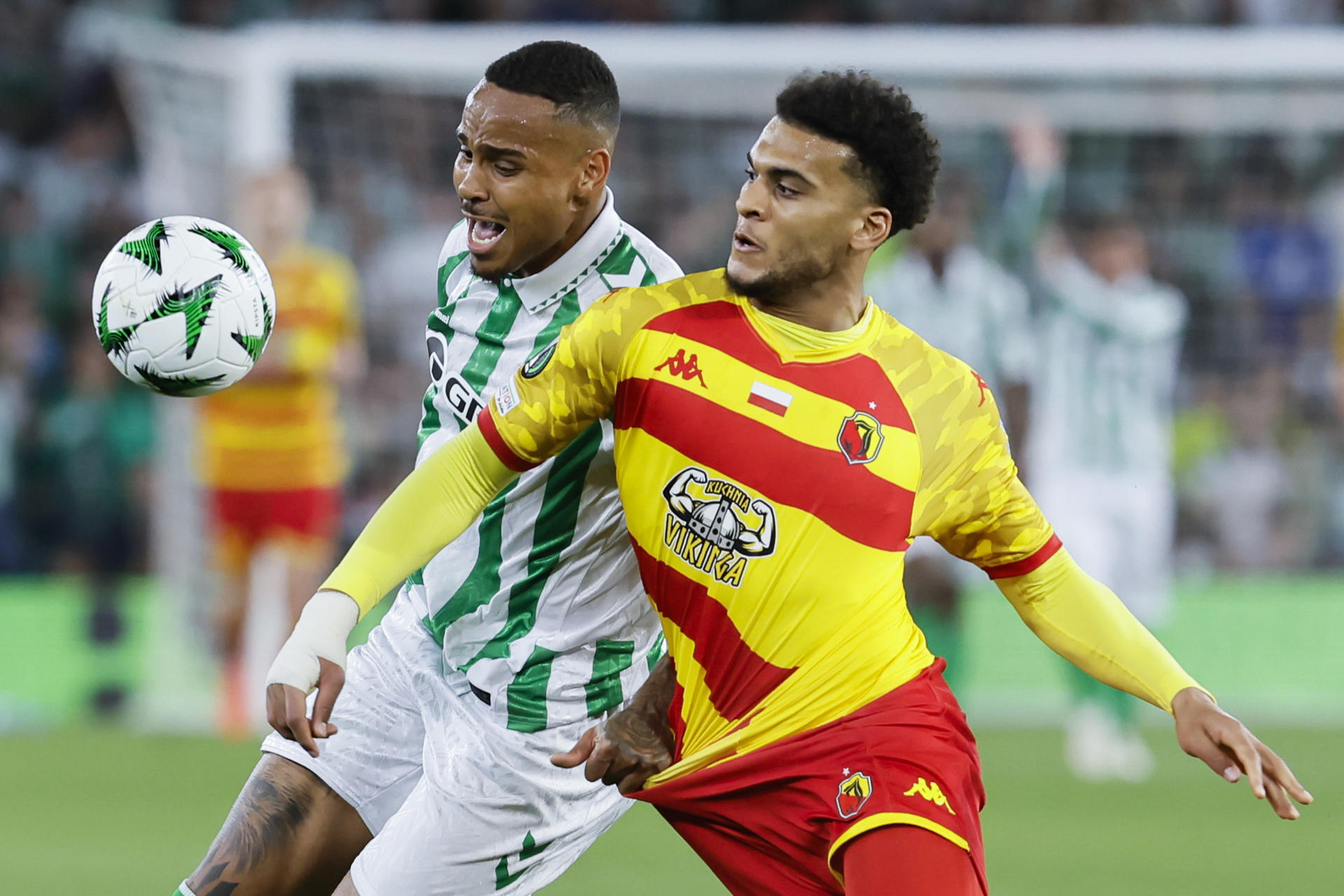 El defensa del Betis Natan Bernardo de Souza (i) pelea un balón con Mohamed Lamine, del Jagiellonia Bialystok, durante el partido de ida de los cuartos de final de la Liga Conferencia que Real Betis y Jagiellonia Bialystok disputan este jueves en el estadio Benito Villamarín, en Sevilla. EFE/José Manuel Vidal