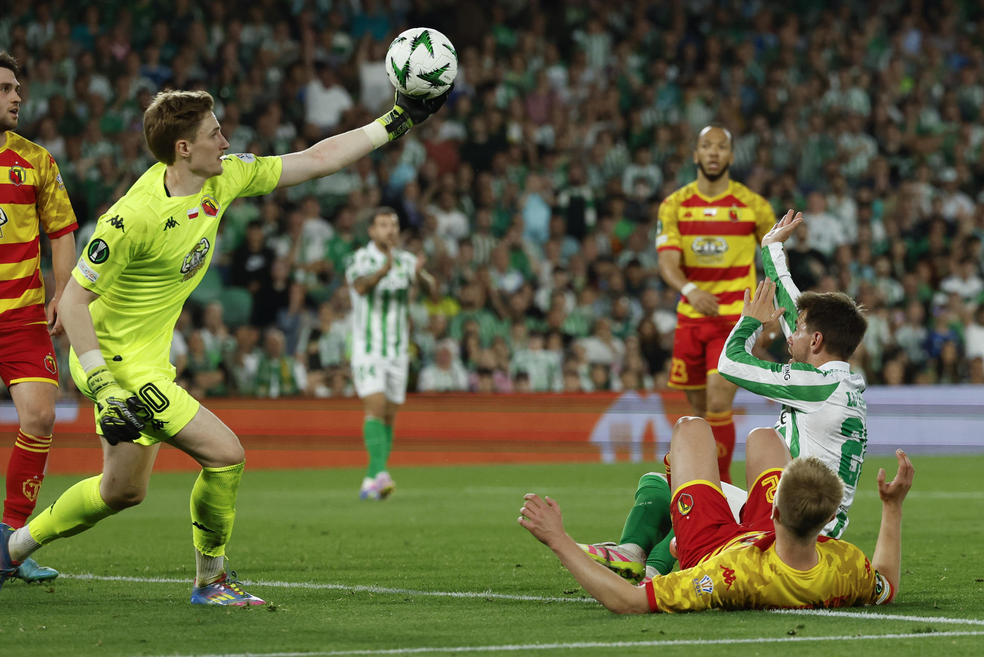 El portero del Jagiellonia Bialystok, Slawomir Abramowicz (i), detiene un balón durante el partido de ida de los cuartos de final de la Liga Conferencia que Real Betis y Jagiellonia Bialystok han disputado este jueves en el estadio Benito Villamarín, en Sevilla. EFE/Julio Muñoz