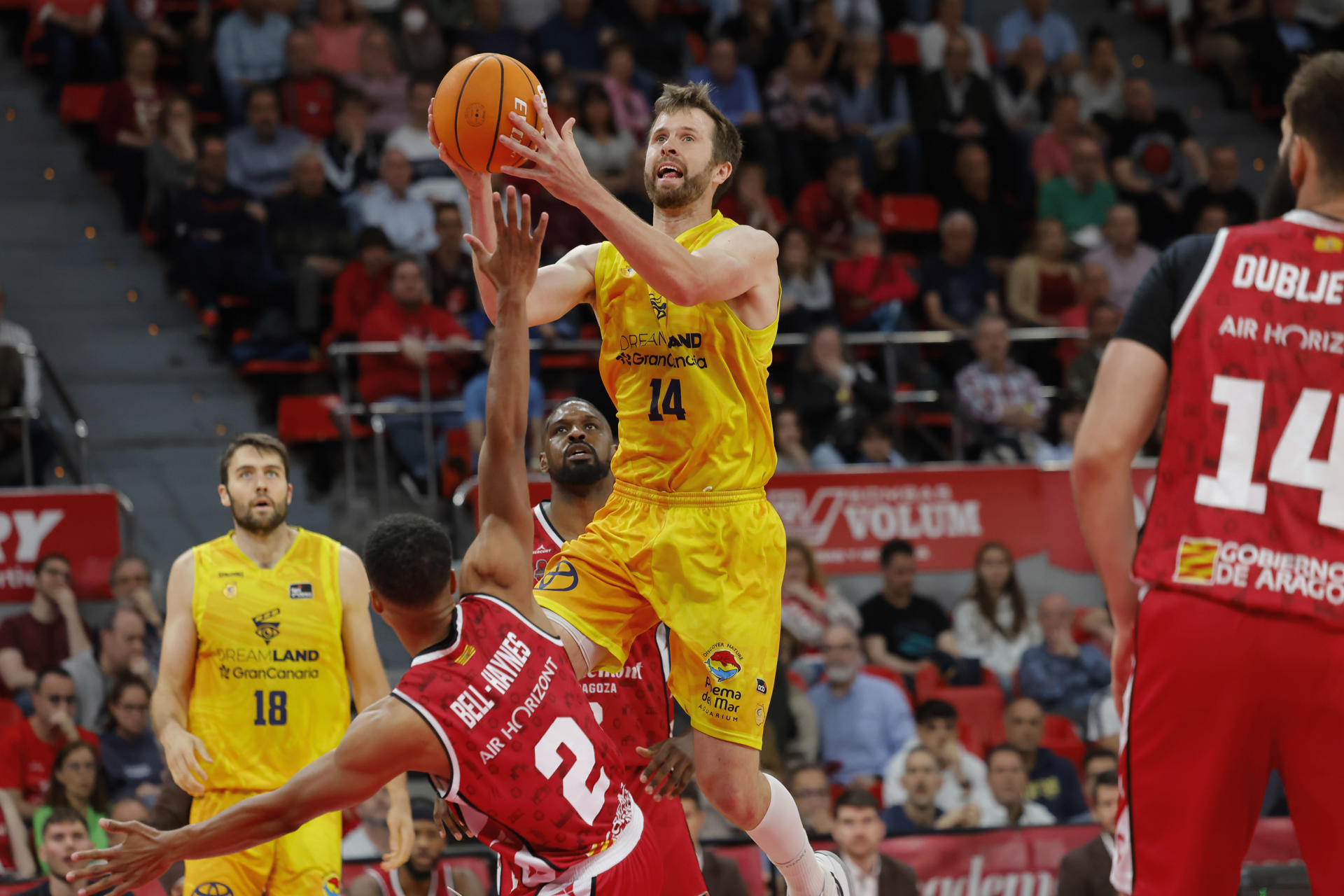 El ala pívot estadounidense del Gran Canaria, John Shurna (c) lanza ante el base canadiense del Casademont Zaragoza, Trae Bell- Haynes (2i), durante el partido de Liga Endesa entre el Casademont y el Gran Canaria, que disputaron en el pabellón Príncipe Felipe de Zaragoza. EFE/ Toni Galán