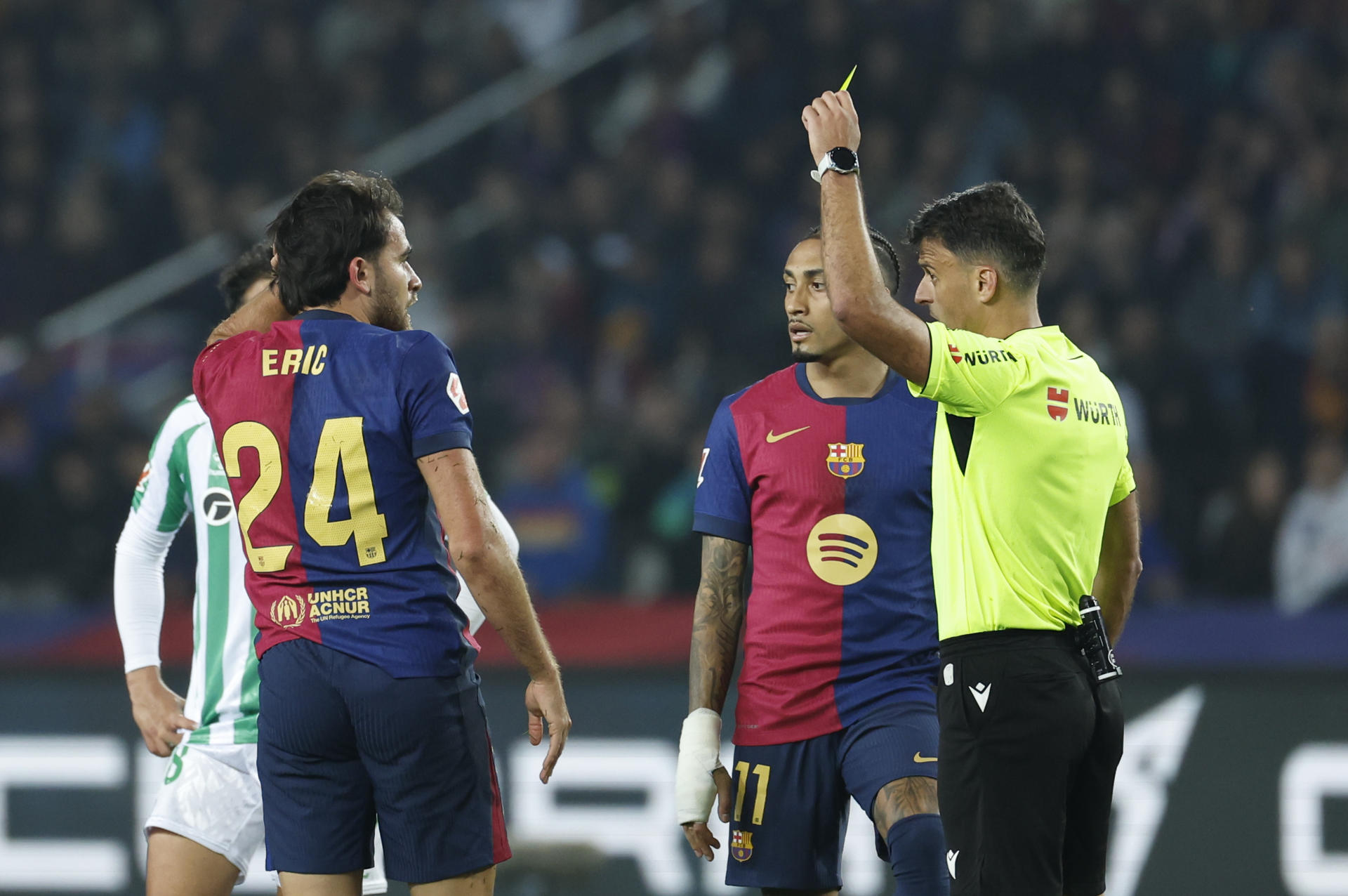 El colegiado Gil Manzano muestra tarjeta amarilla al defensa del FC Barcelona, Eric García, durante el encuentro correspondiente a la jornada 30 de Laliga EA Sports que disputaron FC Barcelona y Betis en el Estadio Olímpico Lluis Companys de Barcelona. EFE / Toni Albir