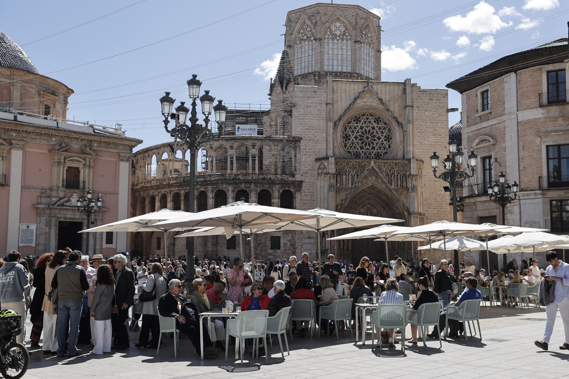 Numerosas personas disfrutan del sol y las altas temperaturas este sábado en la plaza de la Virgen de Valéncia. EFE/Manuel Bruque