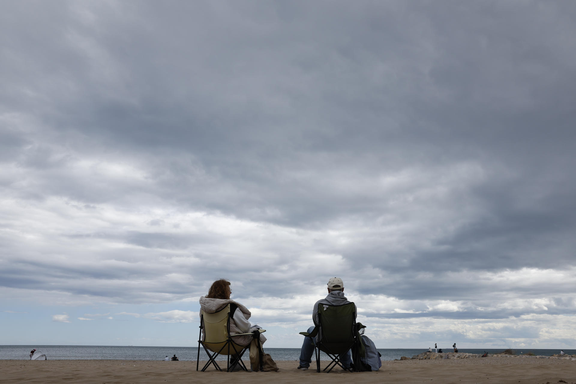 Una pareja conversa este sábado en una playa de Valencia. El frente frío que ha entrado por Galicia trae un final de Semana Santa marcado por la inestabilidad meteorológica, con fuerte viento, precipitaciones en el centro y mitad oriental peninsular, que podrían ir acompañadas de tormentas, y granizo en zonas del nordeste. EFE/ Ana Escobar