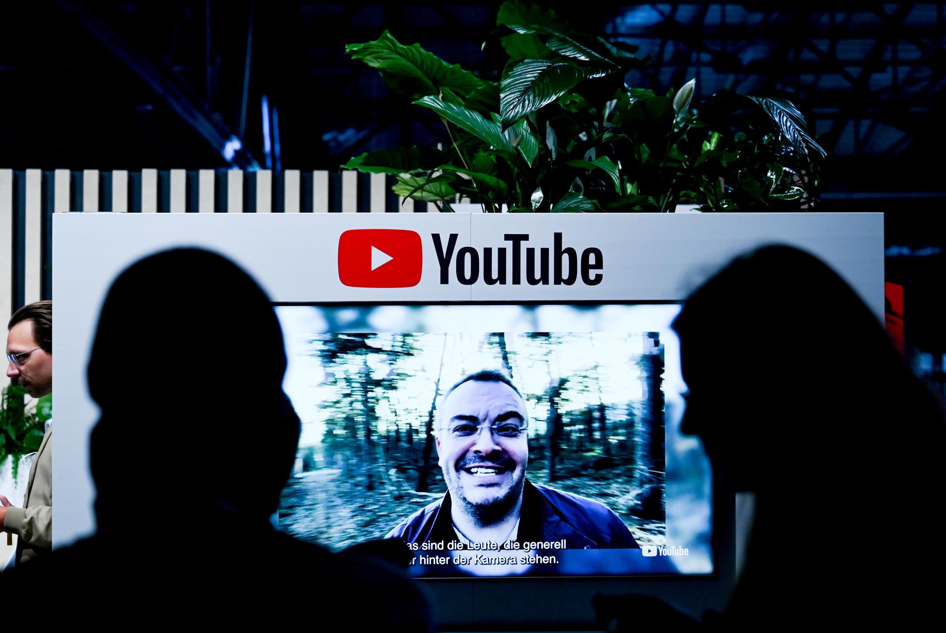 Visitantes junto a una pantalla con el logo de YouTube en una conferencia digital en Berlín, Alemania (2022). EFE/Archivo/EPA/FILIP SINGER