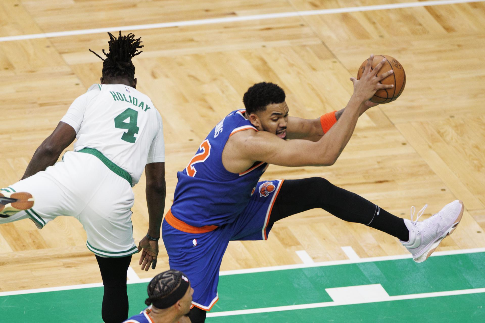 El pívot de Knicks, Karl-Anthony Towns (d), se apodera del balón con una acrobática maniobra que deja fuera de curso al escolta de Celtics, Jrue Holiday (i) durante el partido en Boston que ganaron este lunes los visitantes por 105-108 y que les deja una ventaja por 0-1 en las semifinales del Este de la NBA. EFE/EPA/CJ GUNTHER