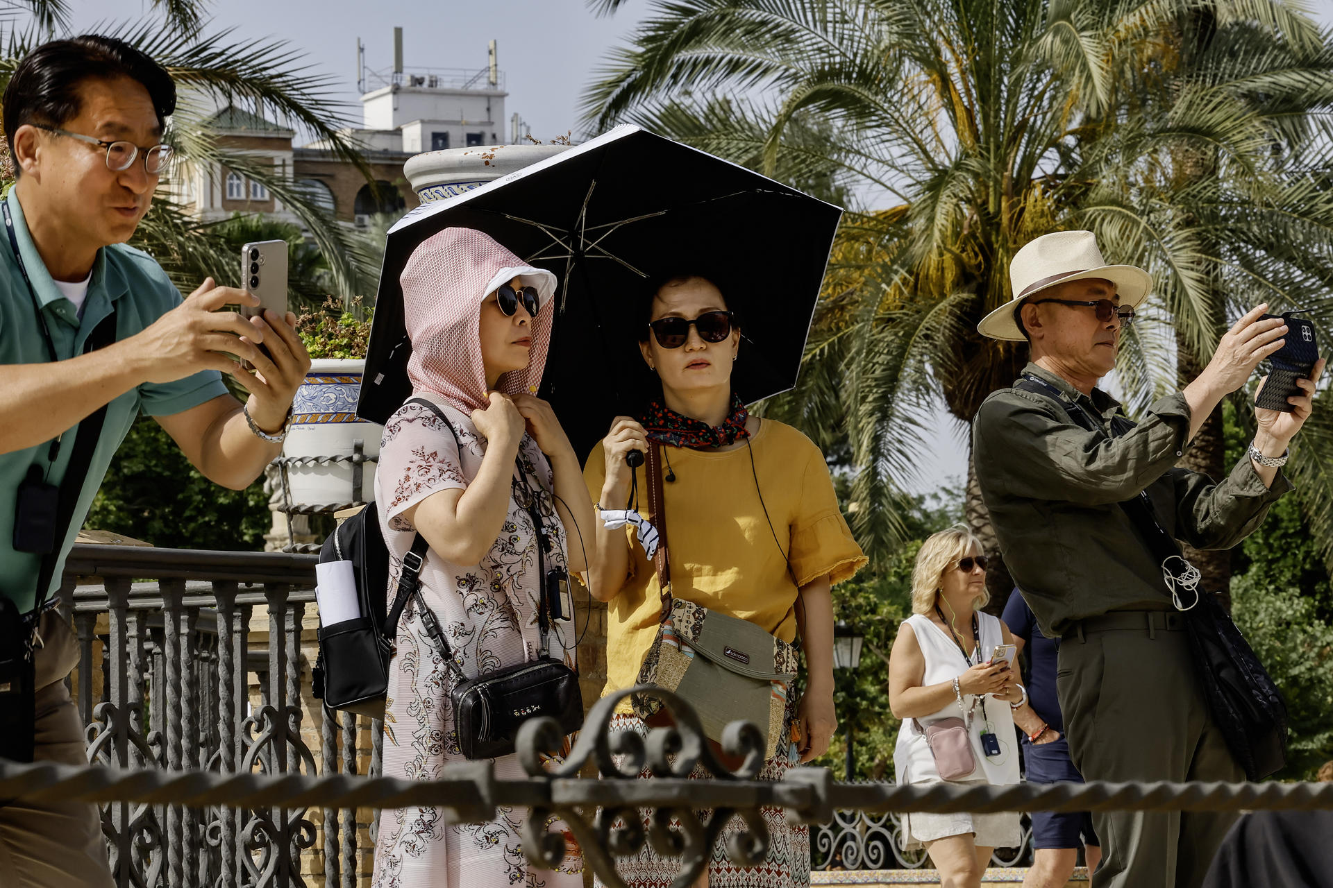 Turistas pasean protegidos con paraguas y pañuelos en la plaza de América de Sevilla, este viernes con temperaturas extremas de hasta 40 grados en Andalucía inusual para el último fin de semana de mayo. EFE /Jose Manuel Vidal