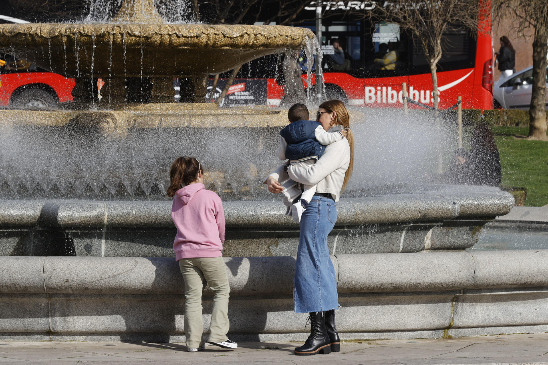 Una madre junto a su dos hijos contemplan una fuente en Bilbao. EFE/Luis TejidoEFE/